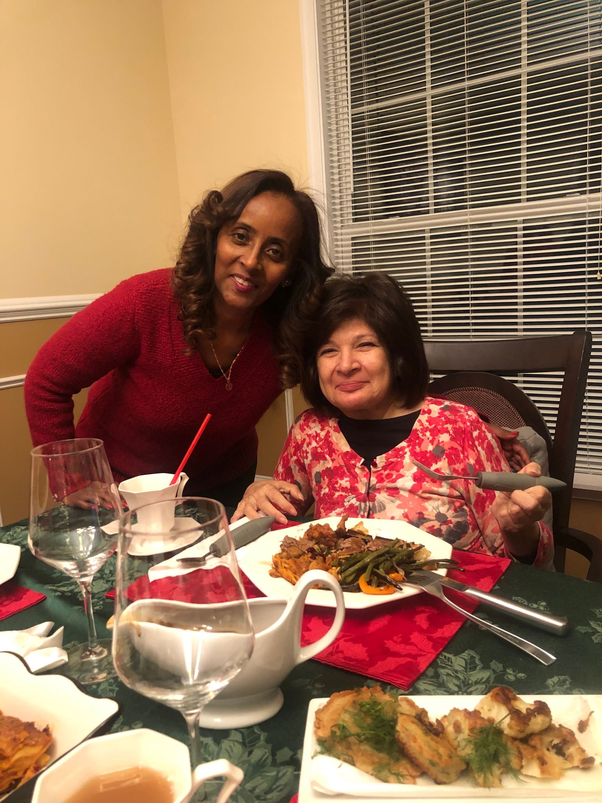 Two people smiling while dining at a table set with food and drinks in a home interior.