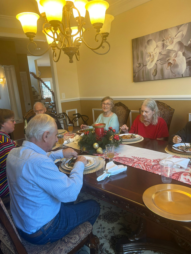 People seated at a dining table with food, ornaments, and a chandelier.