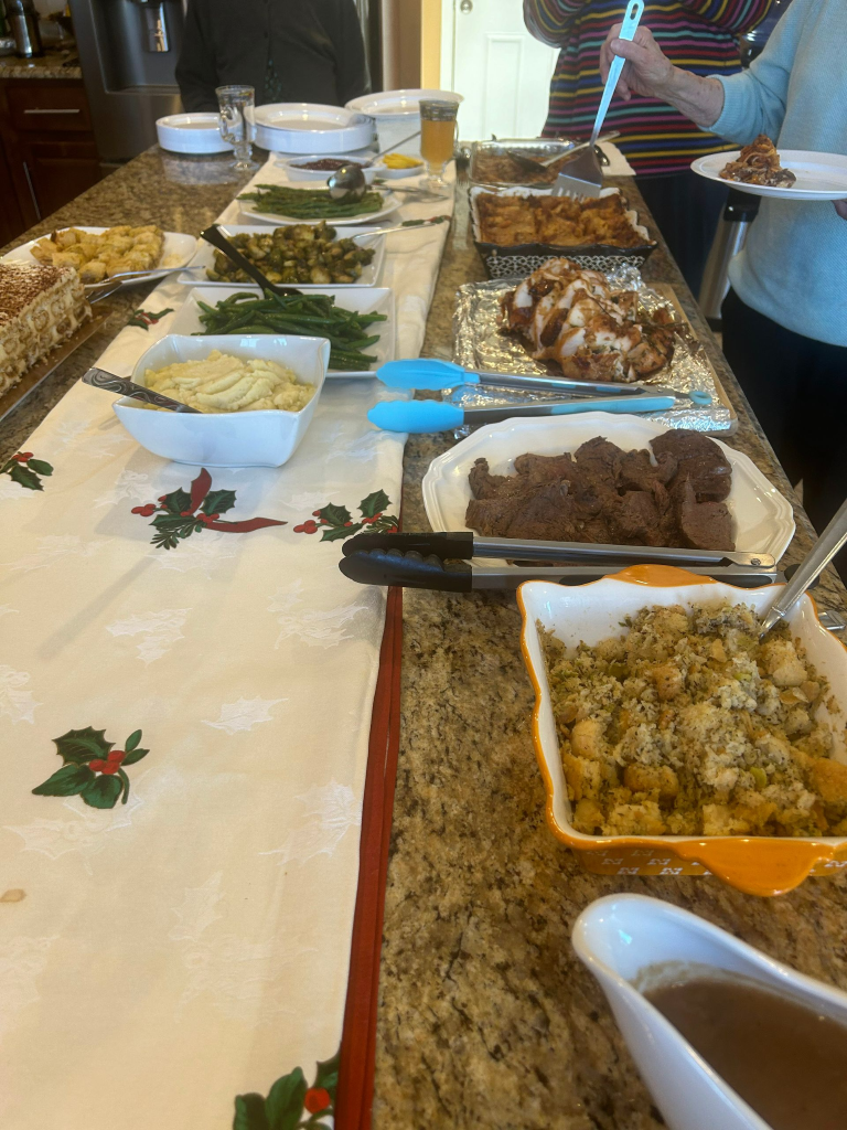Thanksgiving feast laid out on a table, including turkey, sides, and people serving themselves.