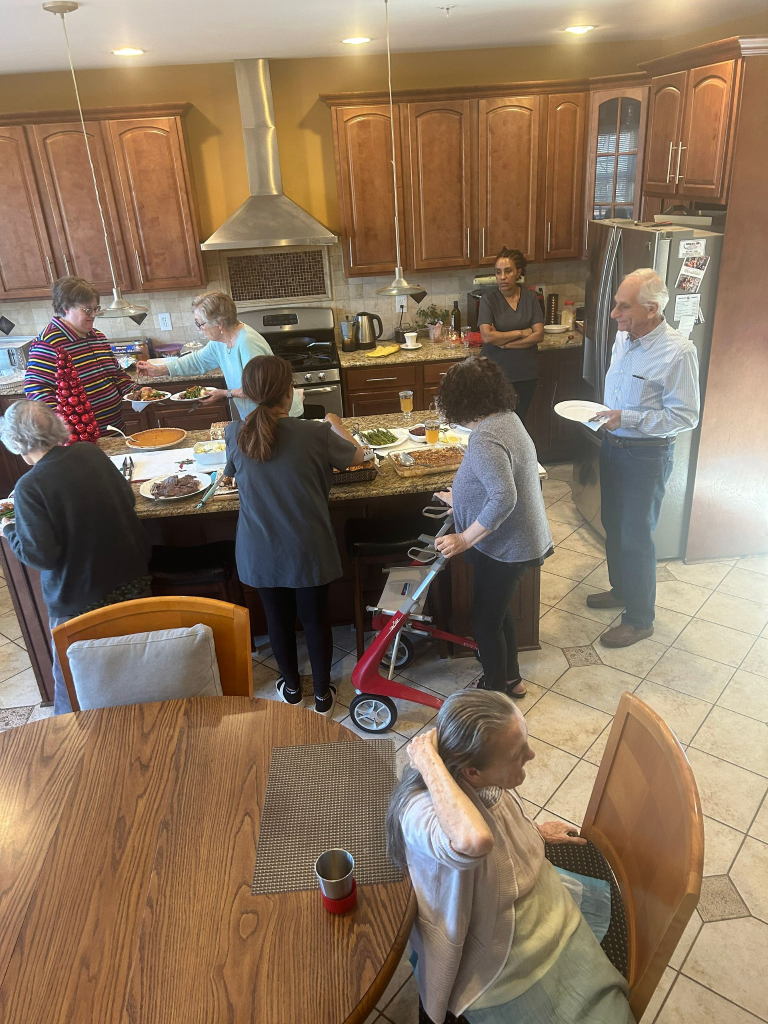 People preparing food in a kitchen with wooden cabinets. Some are at an island counter, others sitting.
