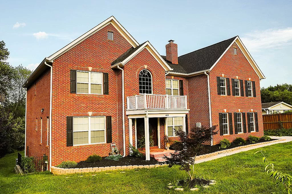 Two-story brick house with a swirling, optical illusion effect on the left side, surrounded by a green lawn.