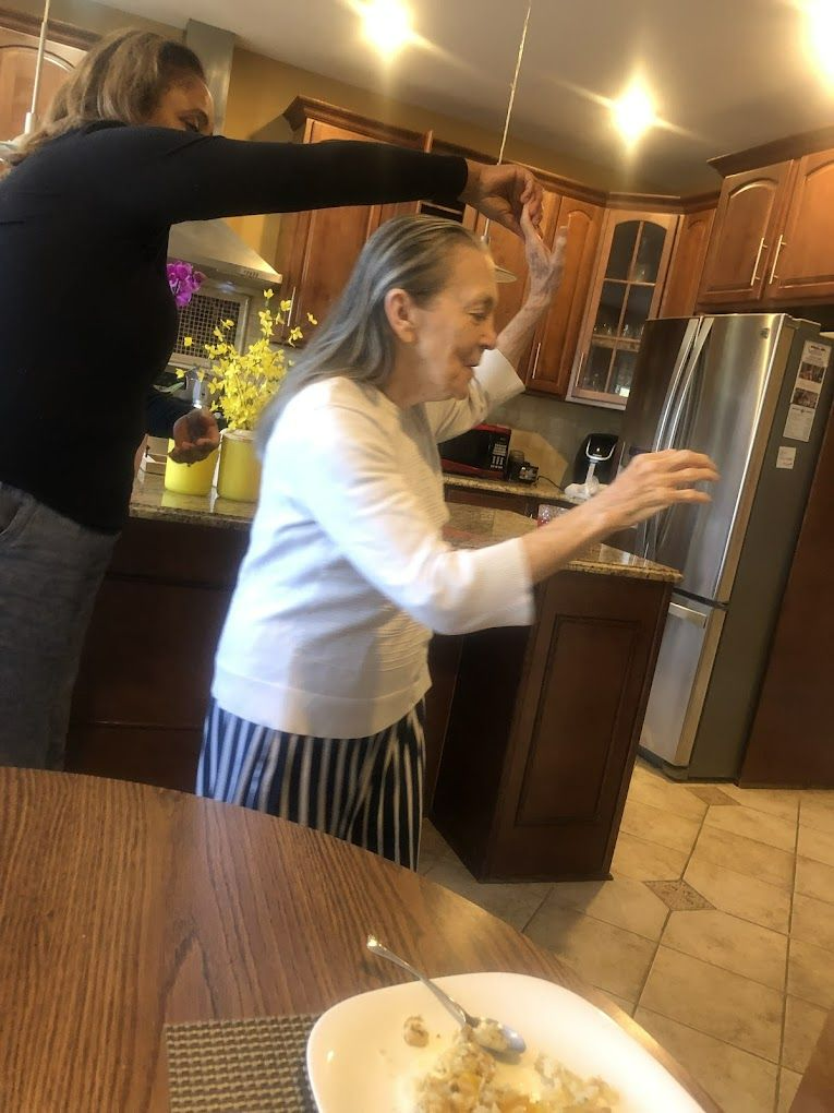 Woman in kitchen reaching up, another person's hand above her.  Smiling, with food on a plate in foreground.