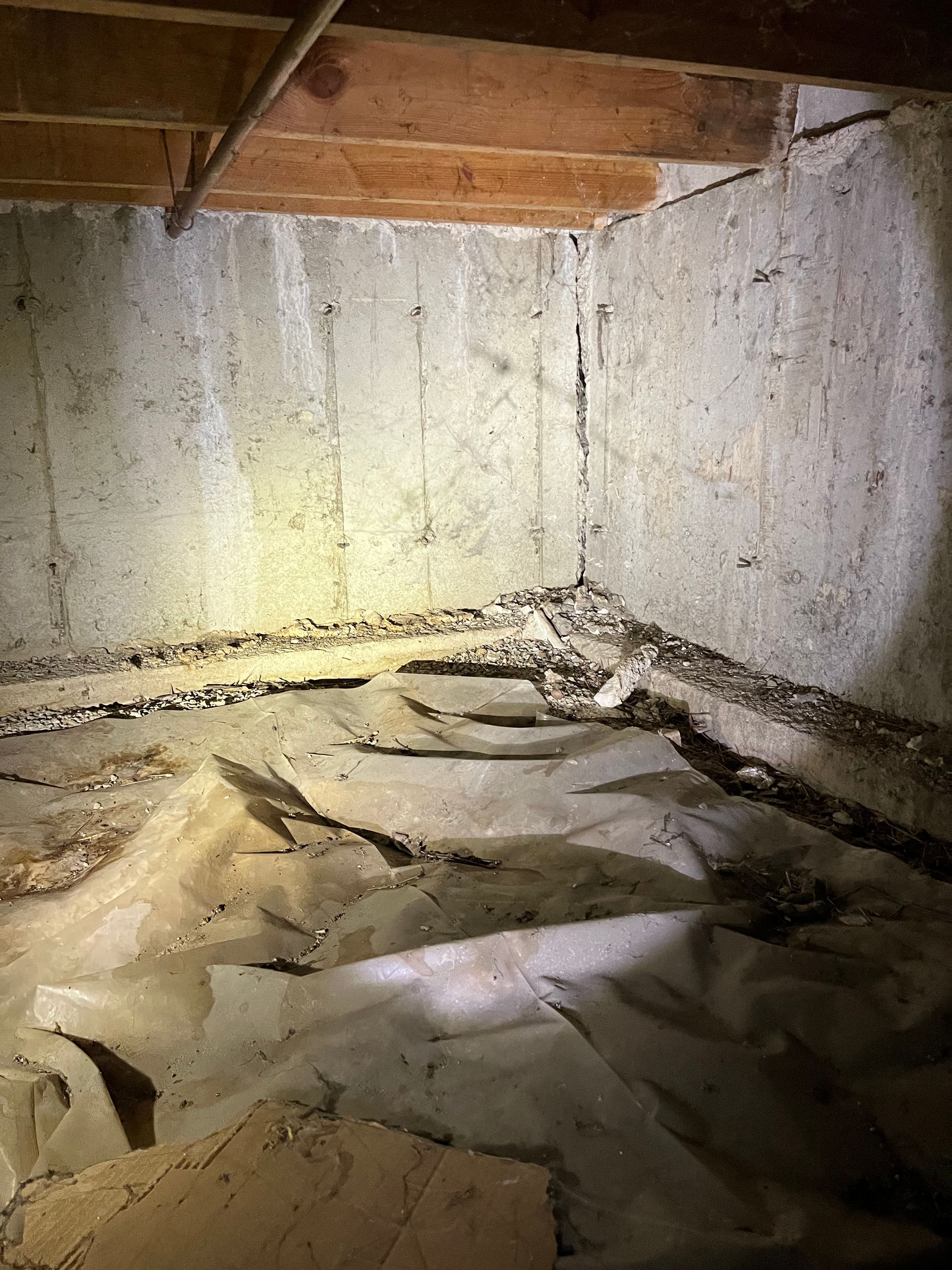 A dim basement corner with concrete walls and a gravel perimeter. Poly sheeting covers the floor.