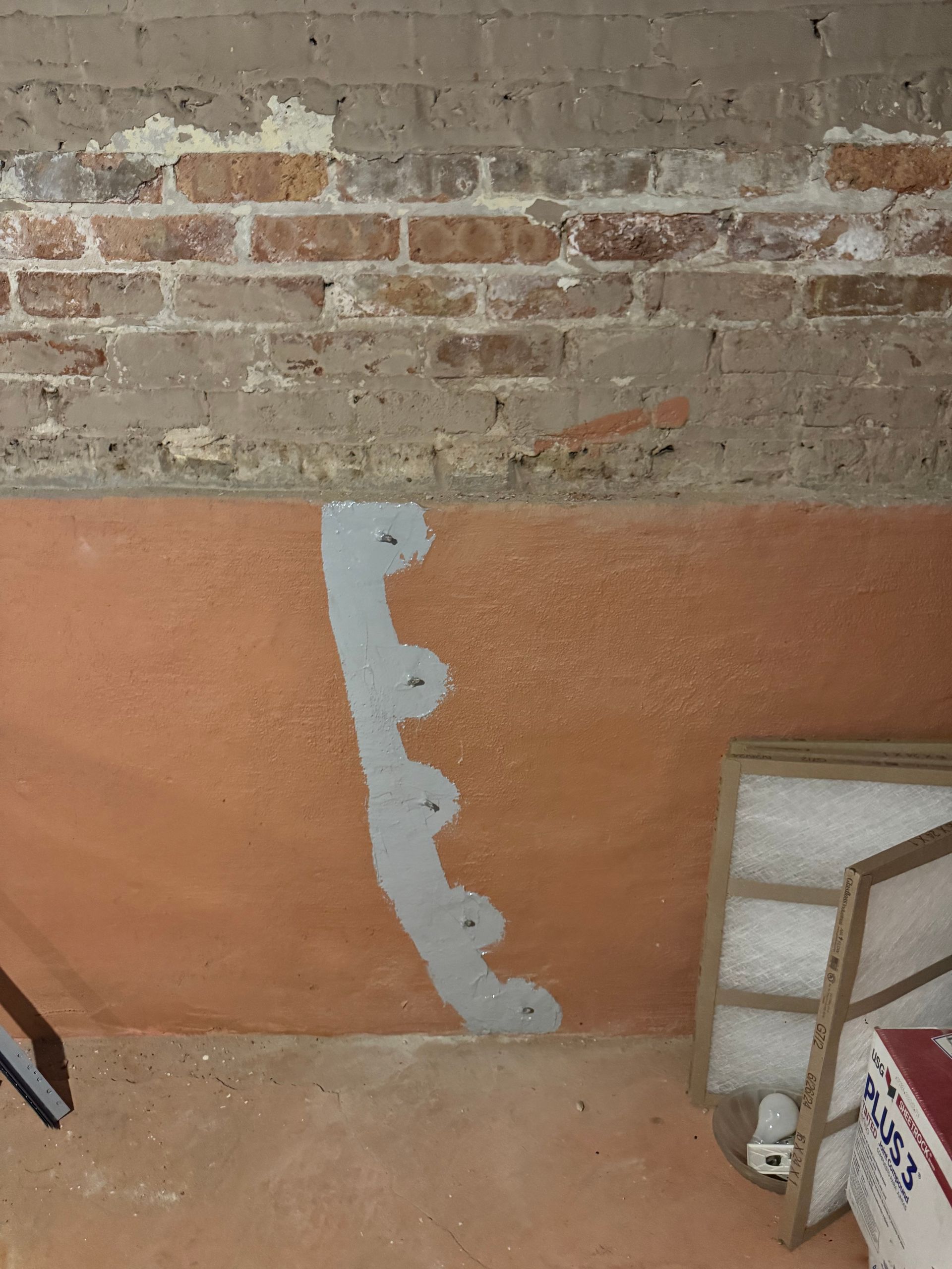 A brick wall with a patched section of light gray concrete. Below, an orange painted wall has a vertical strip of gray material.