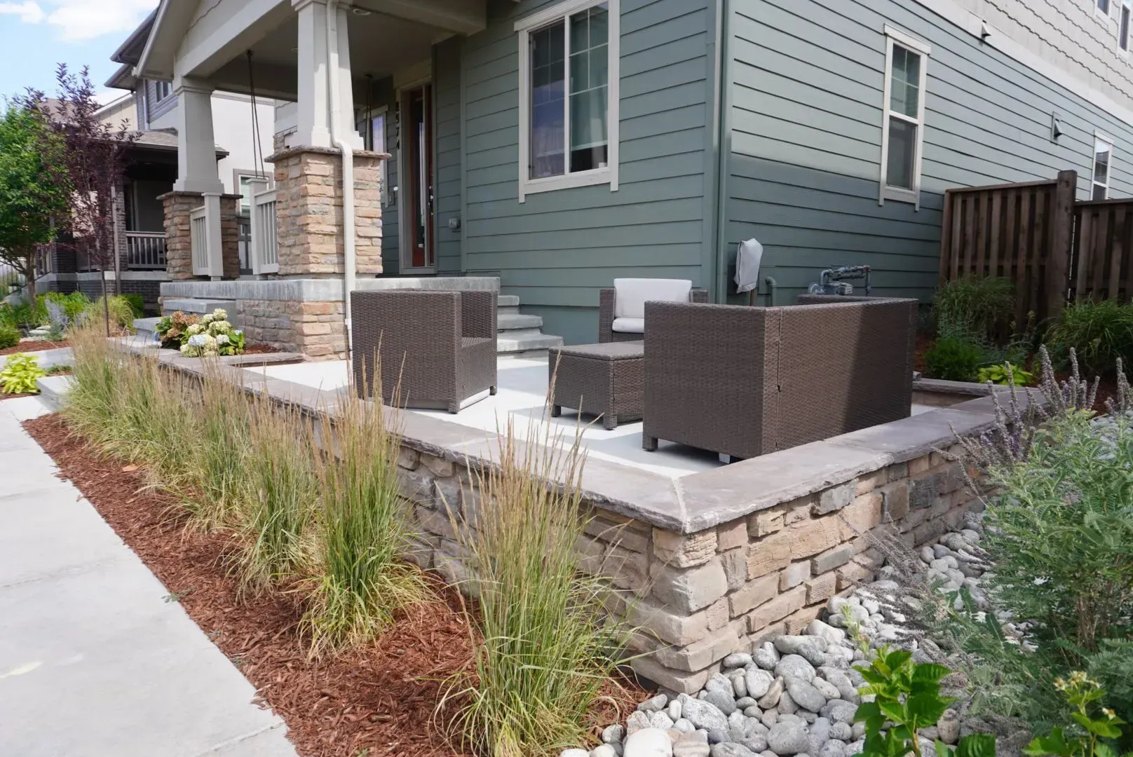 A house exterior with a stone wall, patio furniture, and a landscaped yard.
