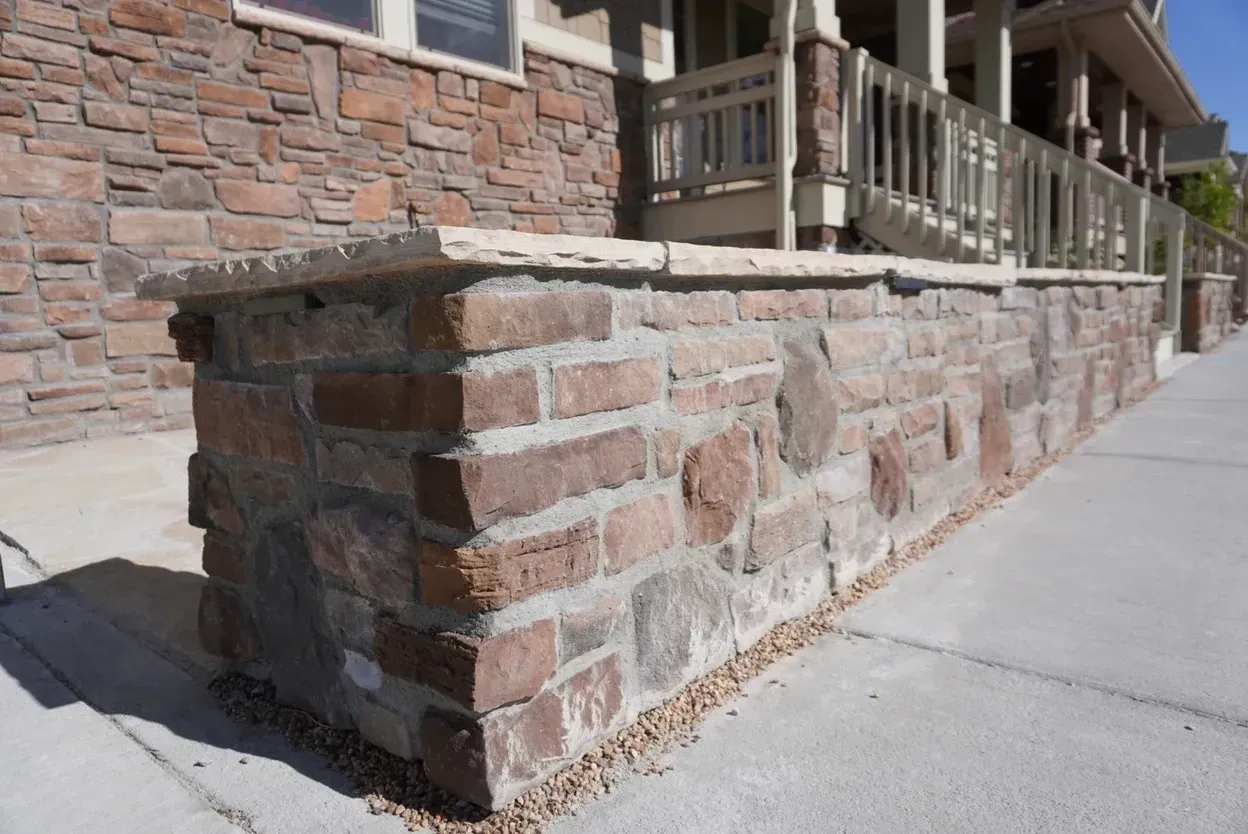 Brick retaining wall with concrete cap, adjacent to a sidewalk and building.