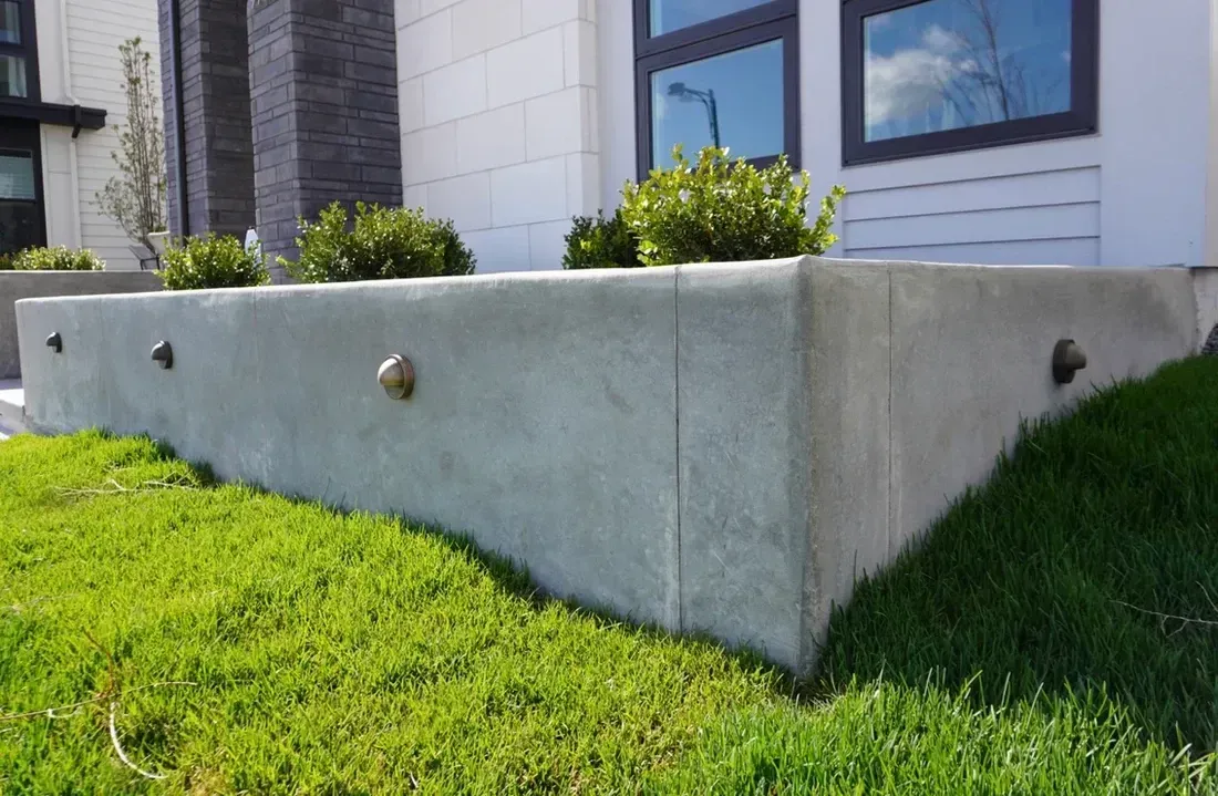 Concrete planter with green grass and shrubs, in front of a modern building with windows.