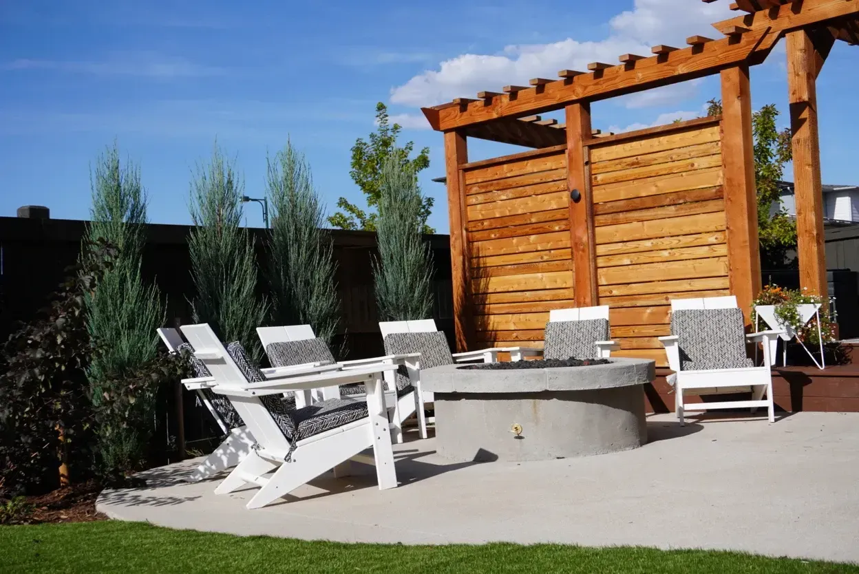 Outdoor seating area with a concrete fire pit, wooden pergola, and Adirondack chairs.