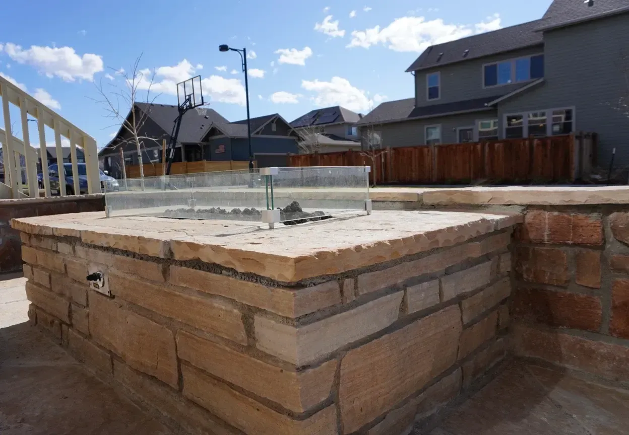 Fire pit made of brick with a glass wind guard in a residential backyard.
