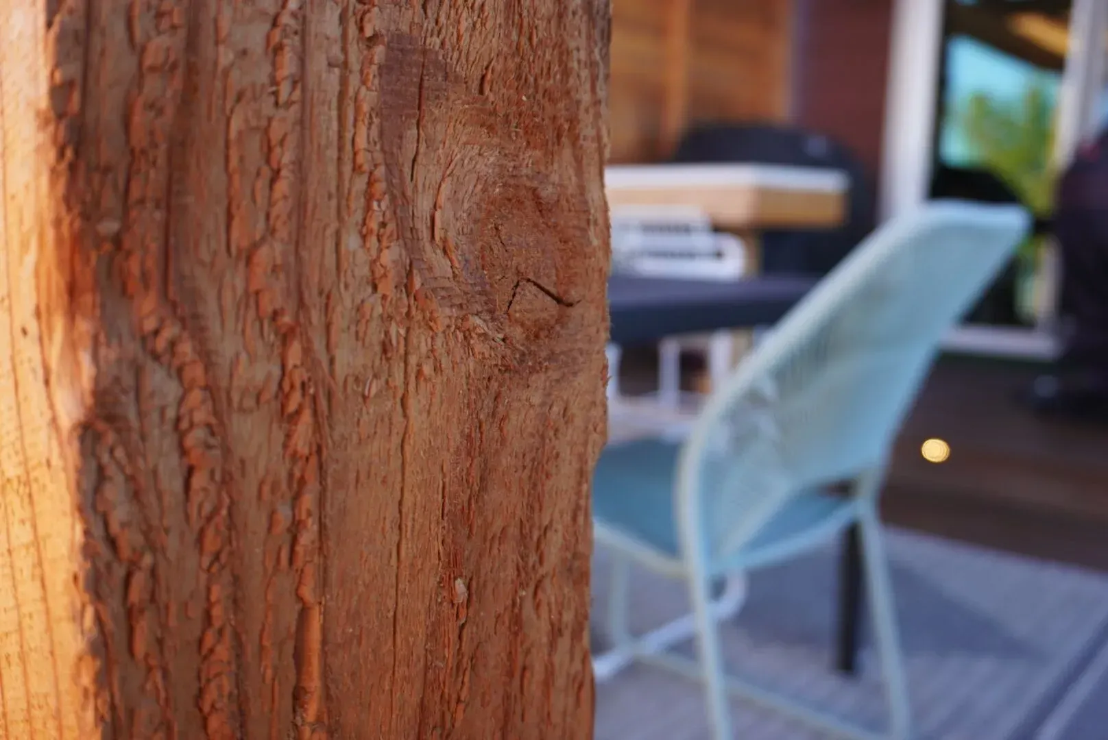 Close-up of a weathered, brown wooden post; a teal chair and patio in soft focus in the background.