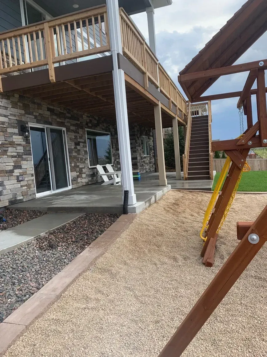Wooden deck with stairs, stone wall, playground with slide, and gravel.