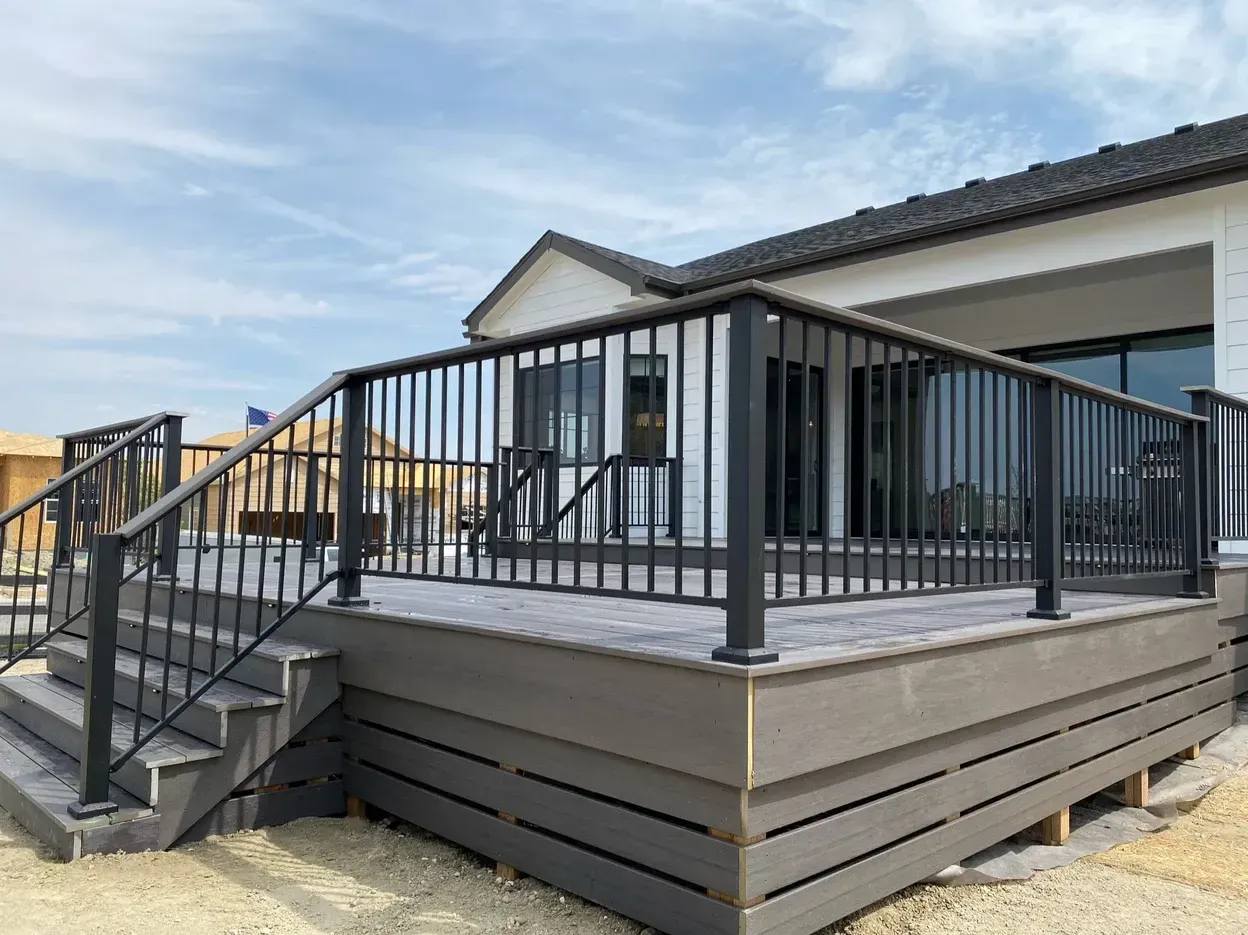 A gray composite deck with black railing and stairs leading to a house.