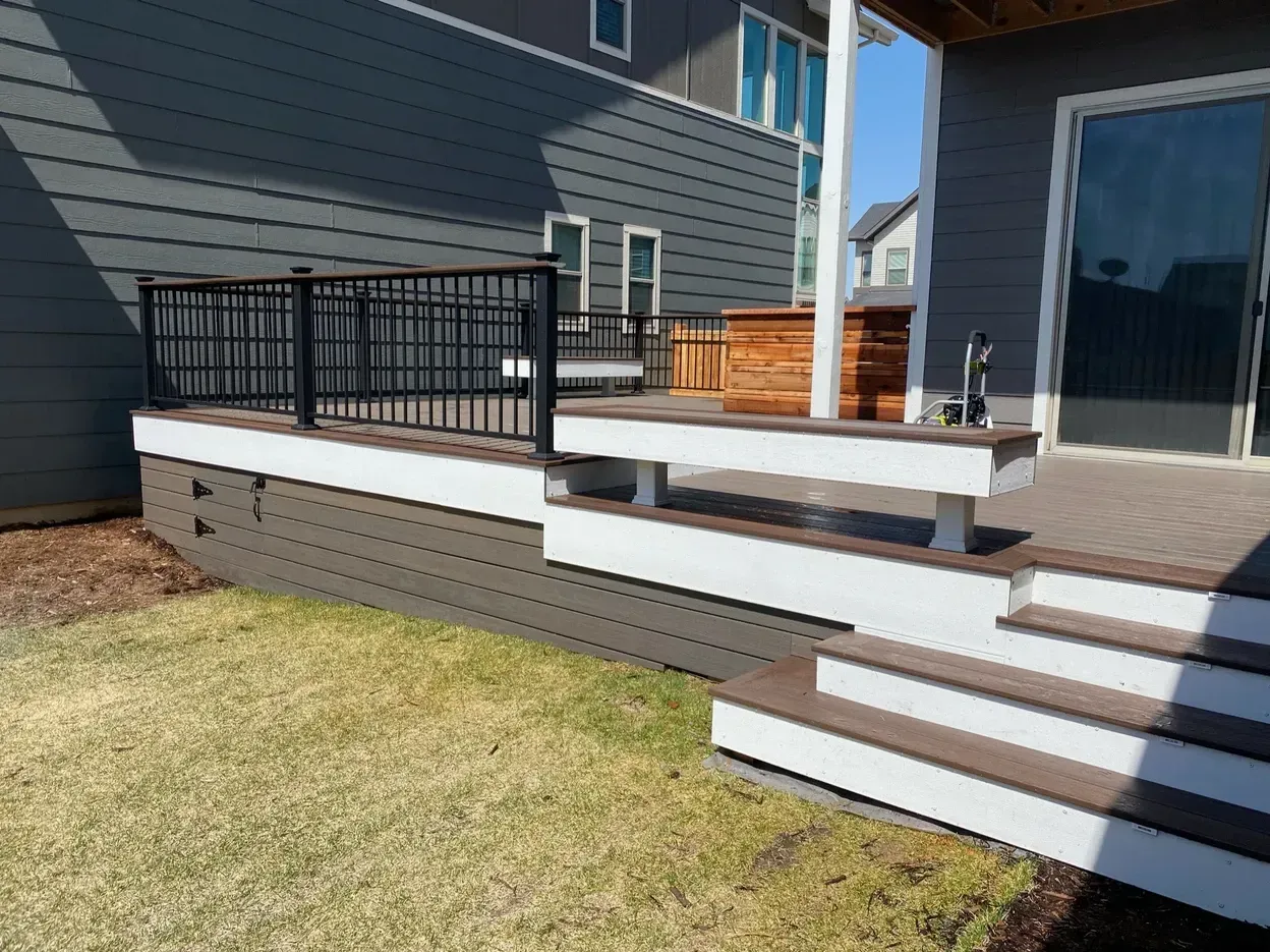 Composite deck with steps and black railing, overlooking a lawn. House in background.