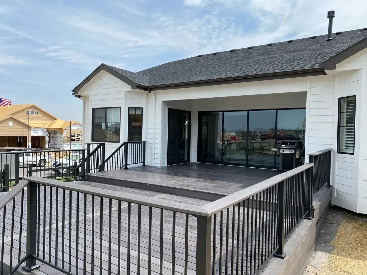 Exterior view of a house with a gray deck and black railings. Large glass doors lead inside.