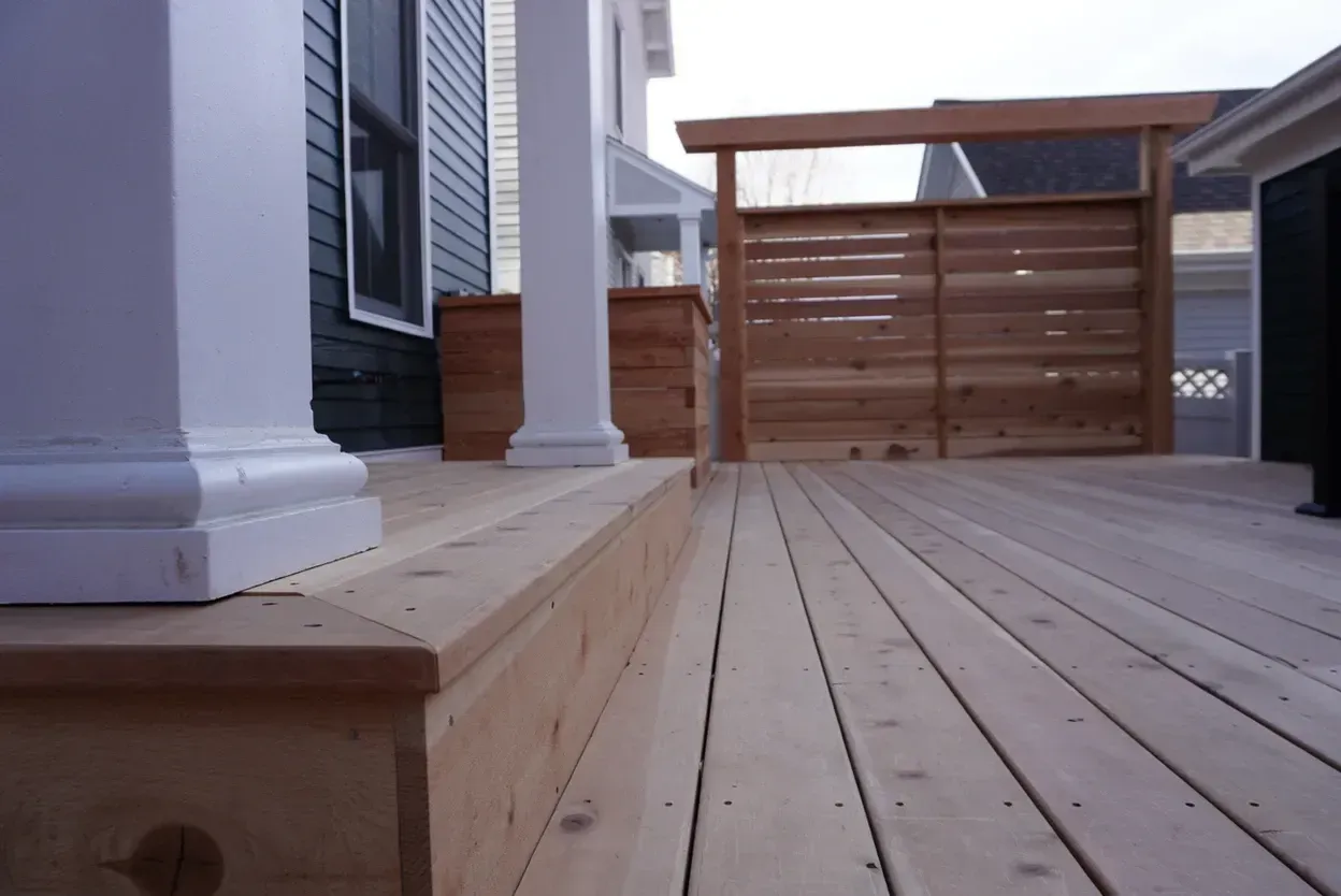 Wooden deck with steps, white columns, and a cedar privacy screen.
