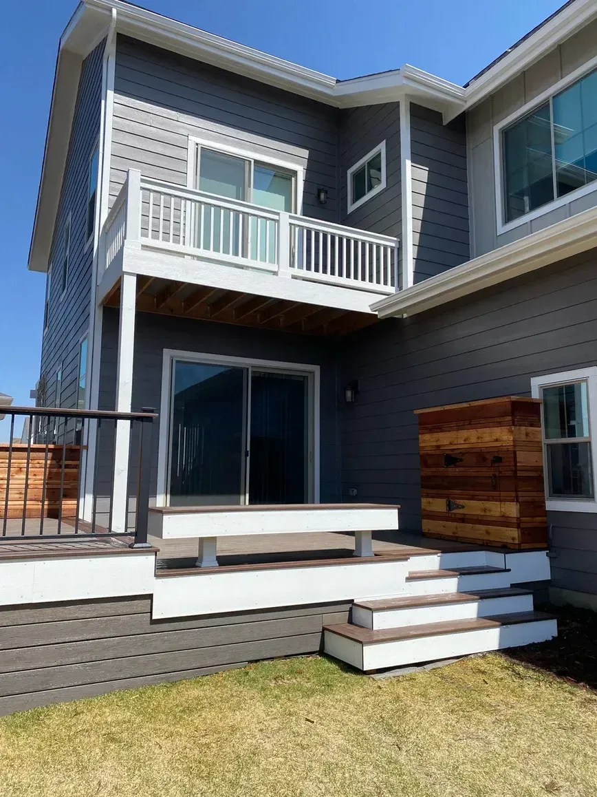 Gray house with multi-level deck and stairs leading to a grassy backyard.