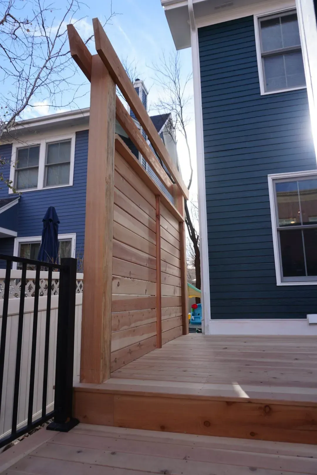 Wooden privacy screen on a deck between two houses; blue and light-colored siding.