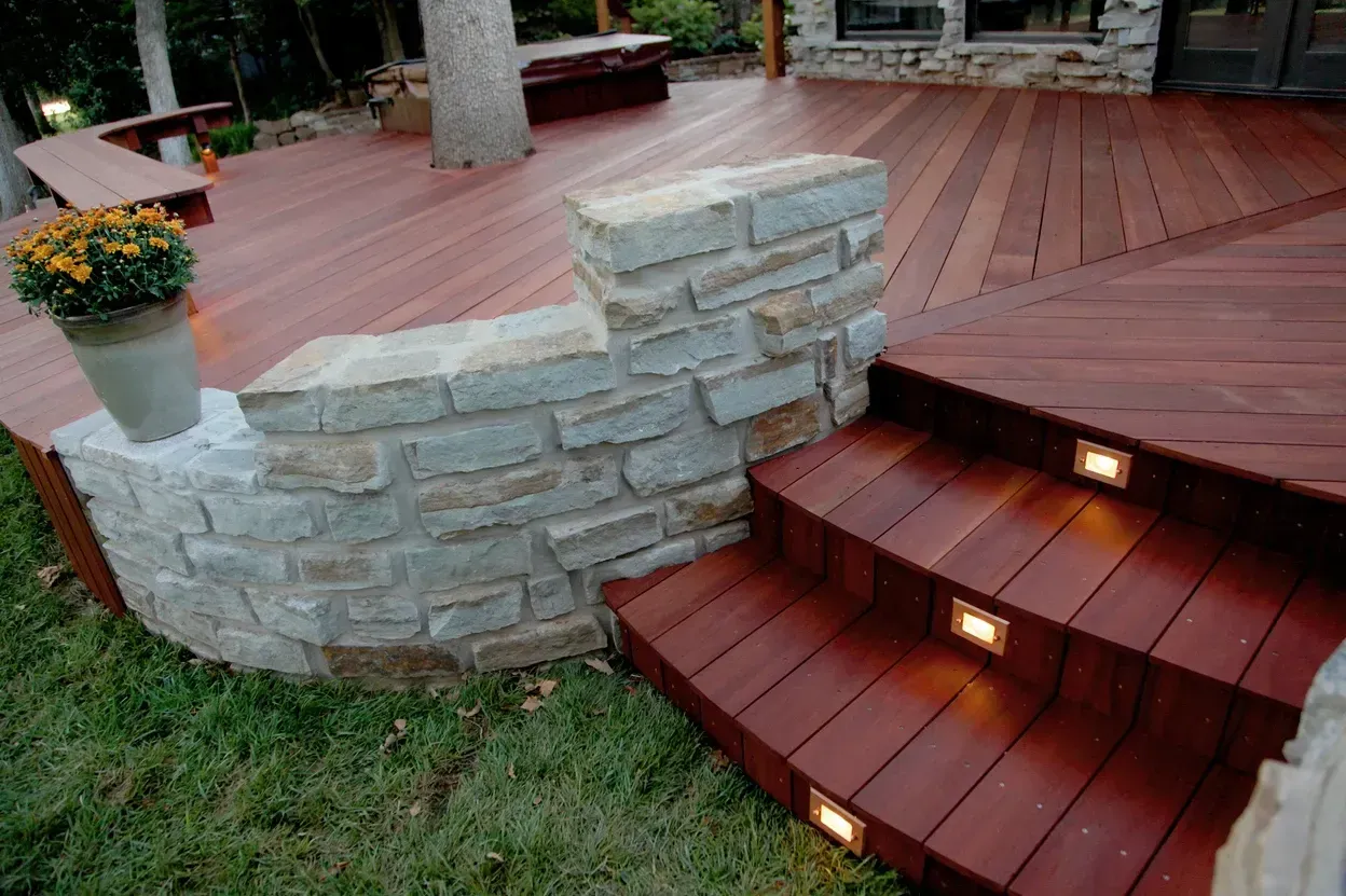 Stone wall and steps lead up to a wooden deck with built-in lighting.