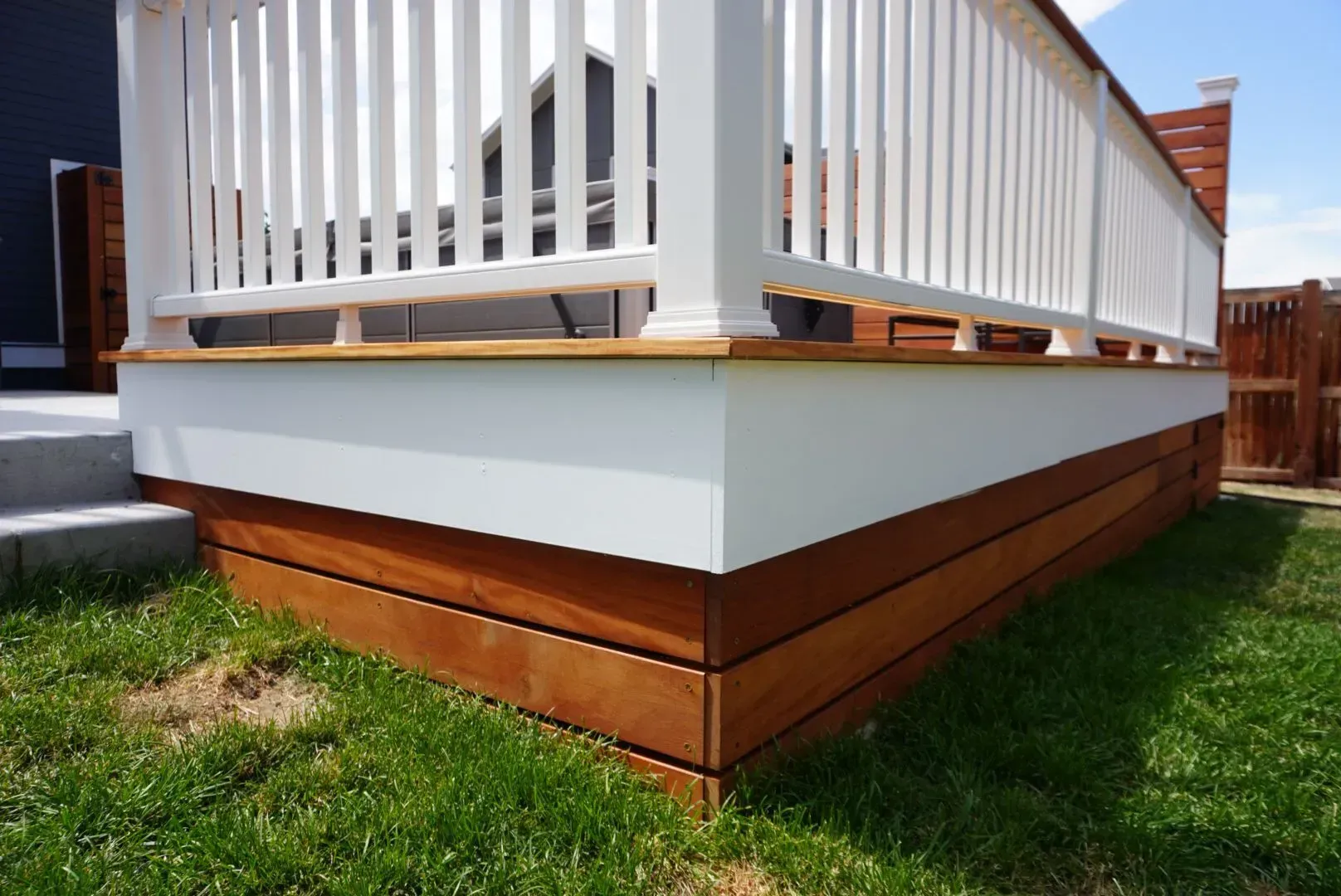 Wooden deck corner with white railing, brown boards, and green grass.
