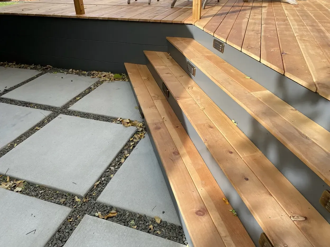 Wooden deck with steps leading down to a concrete patio with gravel.