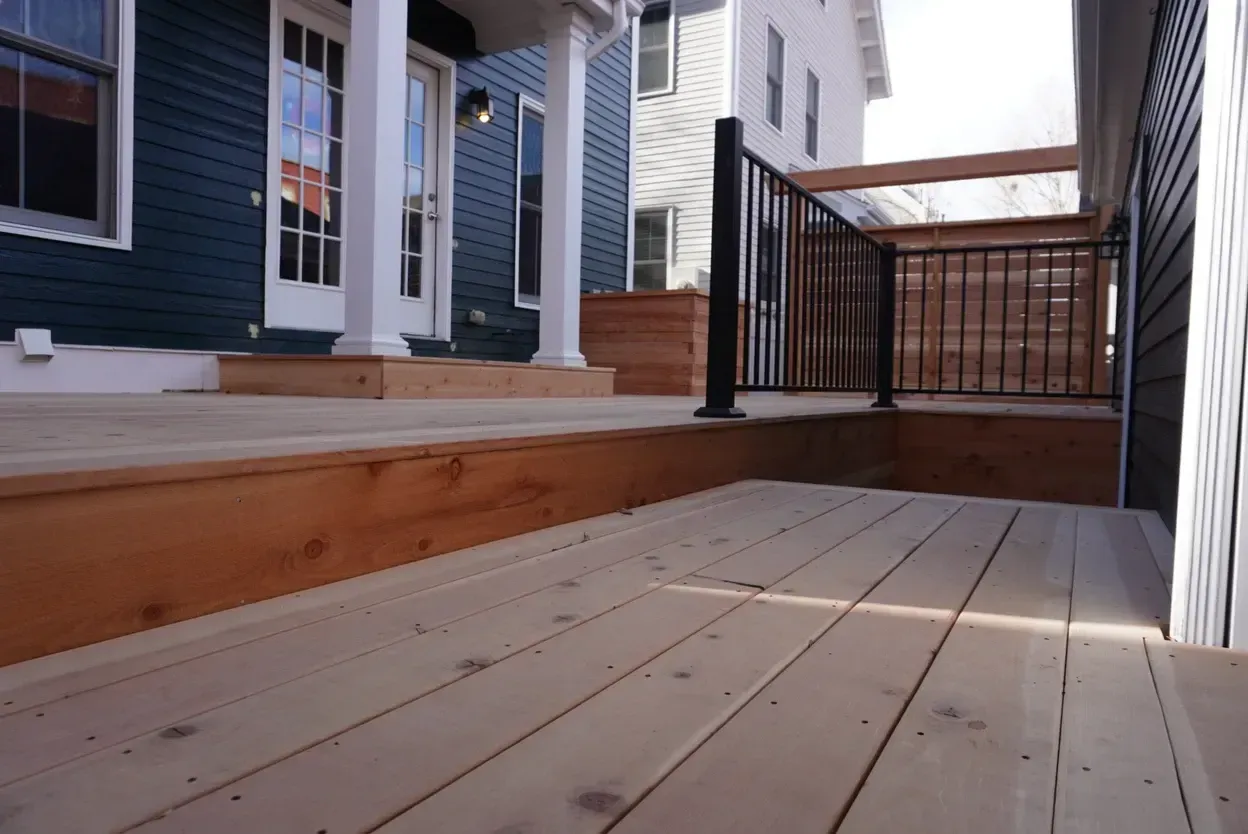 Wooden deck and porch with black railings, leading to a house with blue siding.