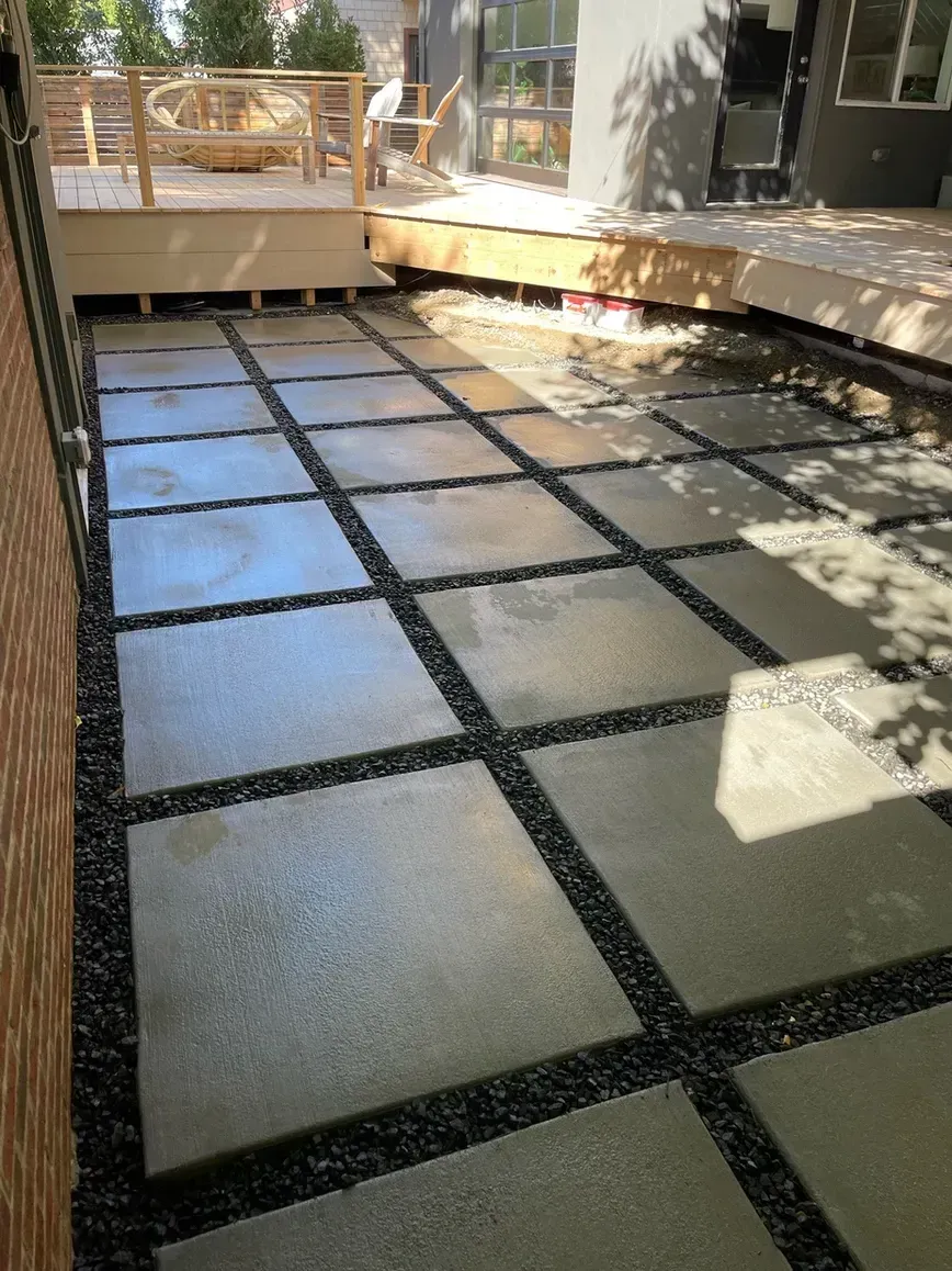 Concrete pavers separated by black gravel in an outdoor patio. Wooden deck in background.