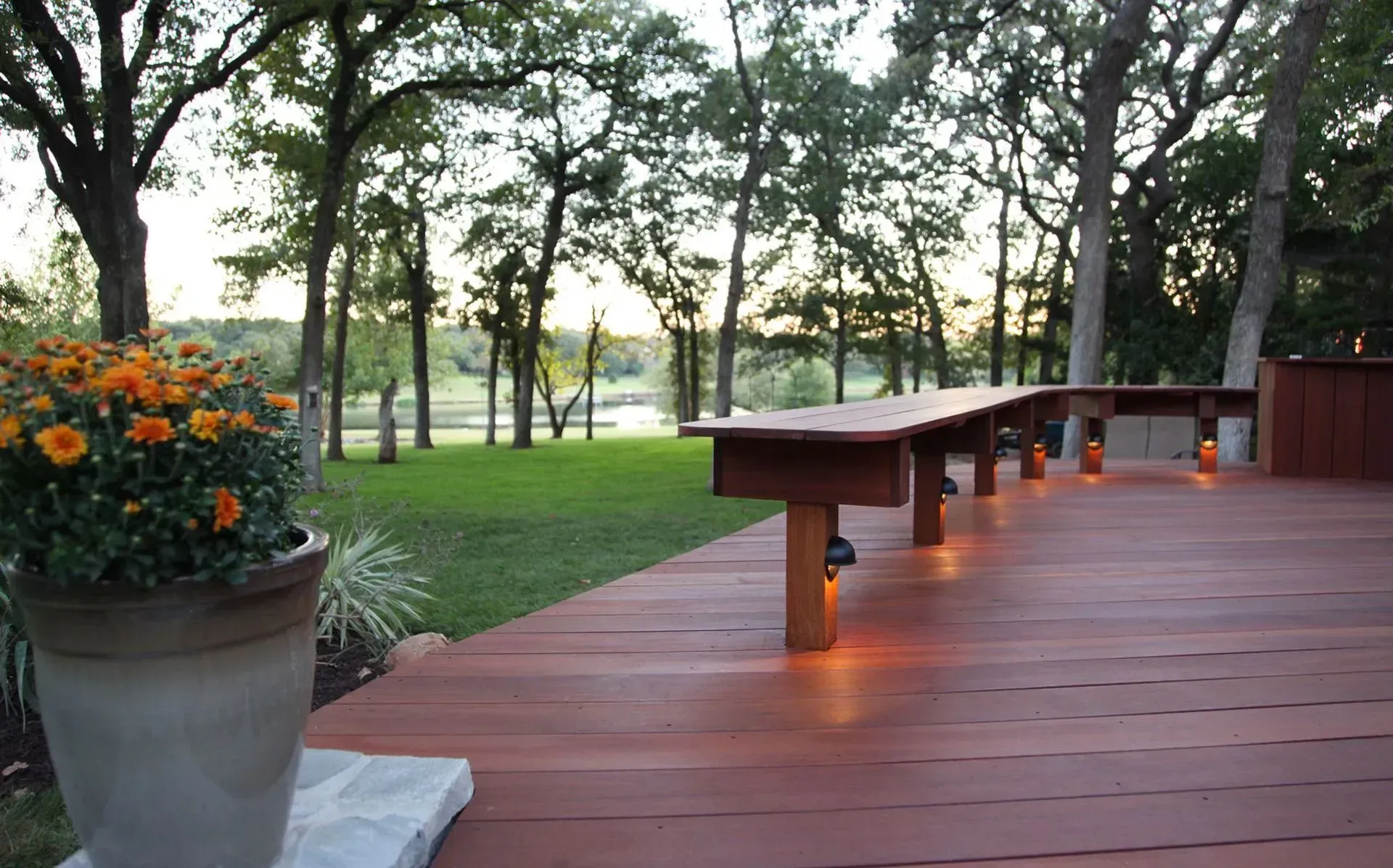 Wooden deck overlooking a green lawn and trees. A flower pot sits on the deck. Dusk.