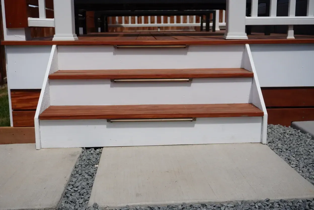 Three wooden steps with metal handrails, painted white risers, leading to a deck.