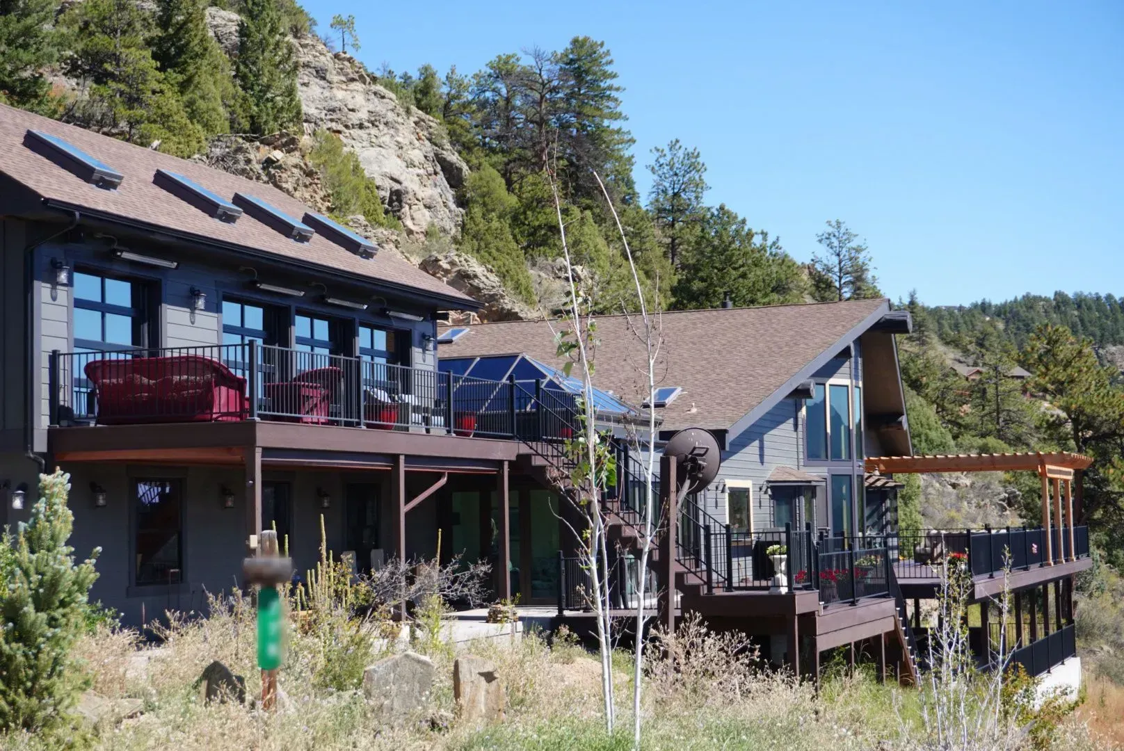 Two houses with decks overlooking a rocky hillside under a blue sky.