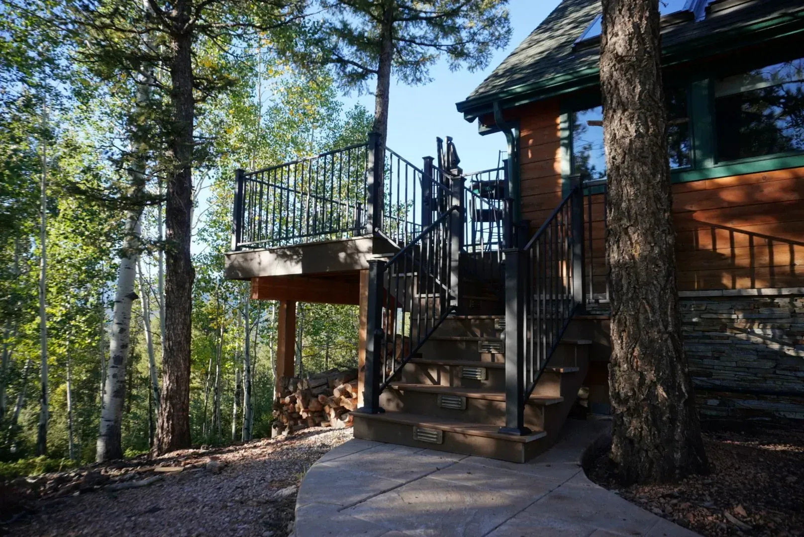 Staircase and deck leading to a cabin-like building in a wooded area, with metal railings.