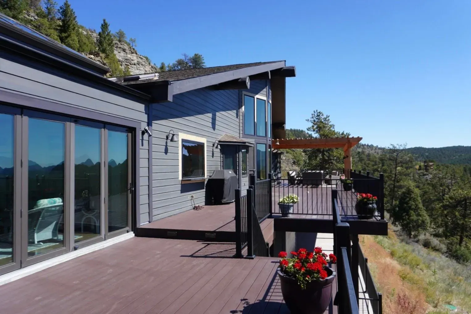 Modern gray house with a deck overlooking a scenic vista, sunny day.