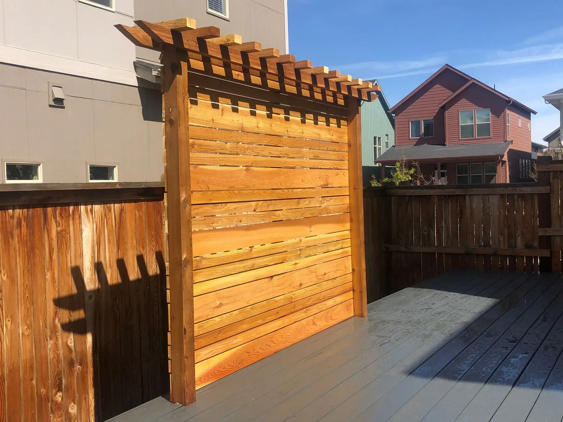 Wooden privacy screen with a pergola top on a deck, with houses in the background.