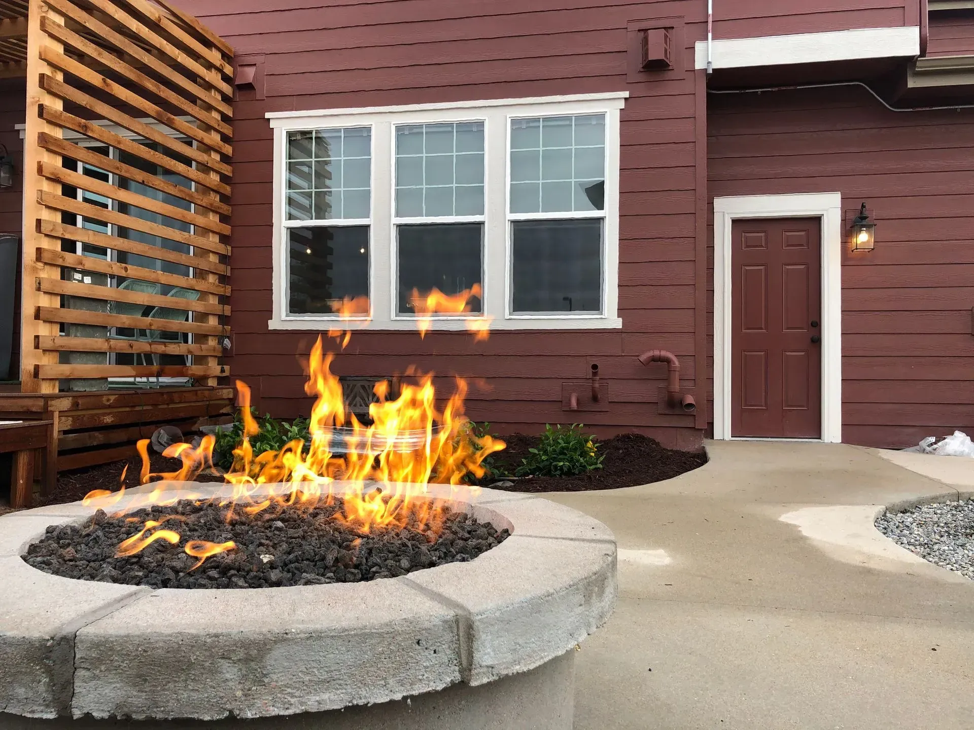 Fire pit with flames in front of a building with a window and door.
