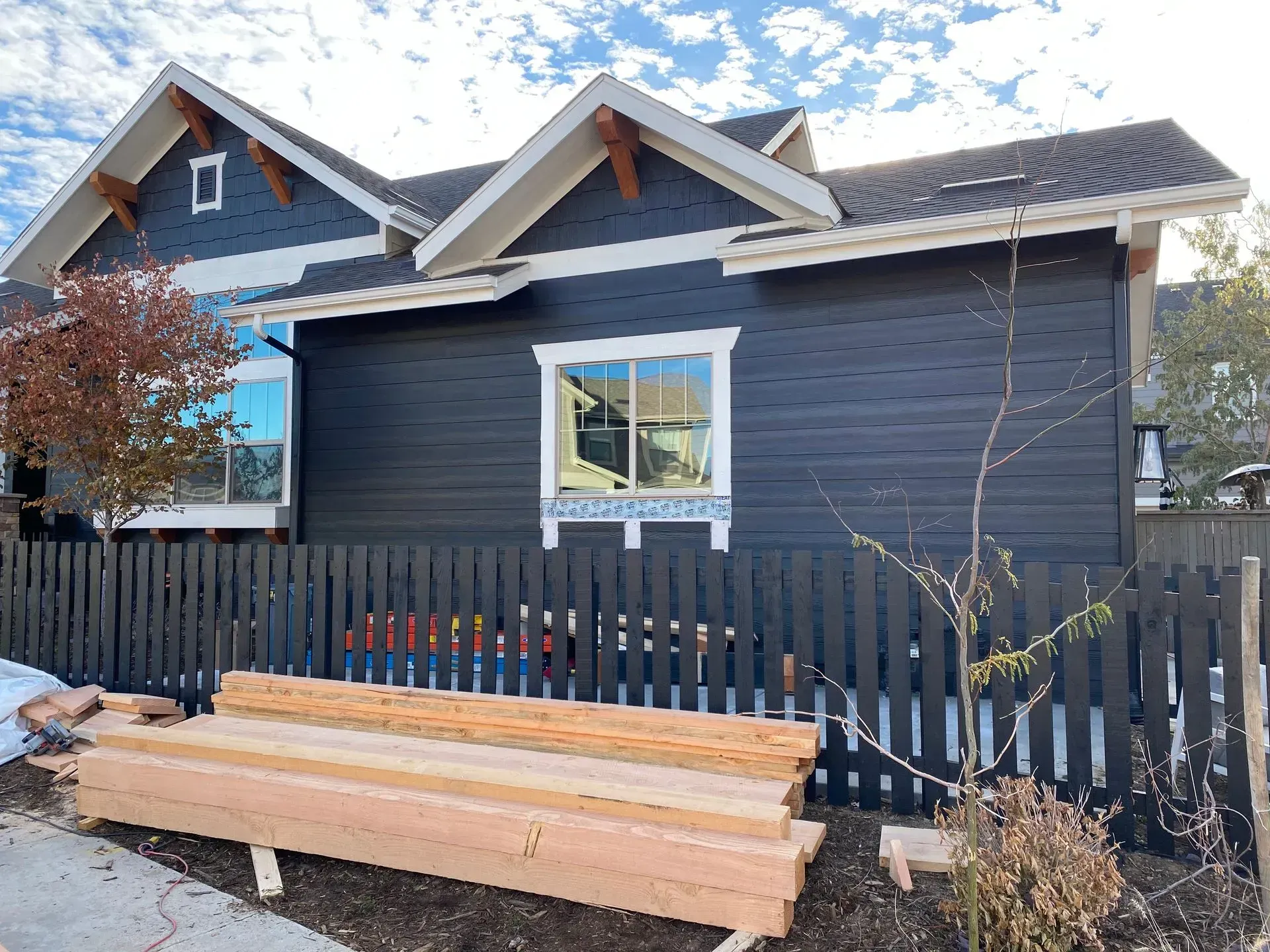 Black house with white trim and fence; lumber in front.