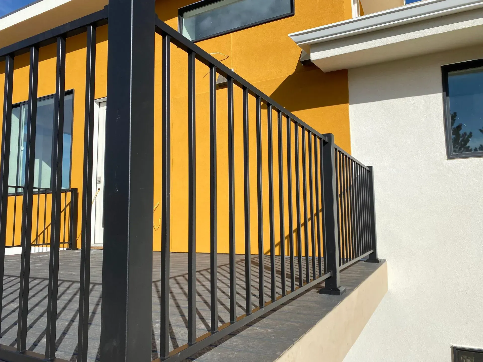 Black metal railing on a deck with a yellow and white building background.