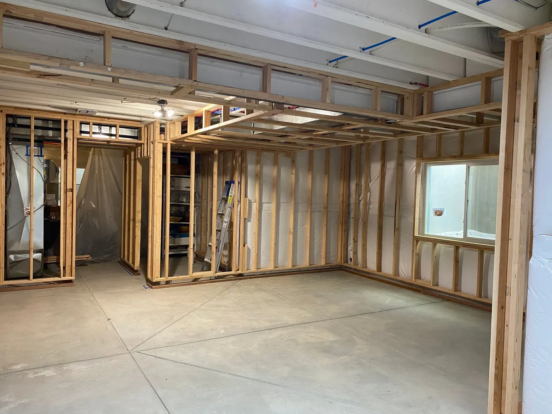 Interior of a room under construction; wooden framing on concrete floor, with a window and doorway.
