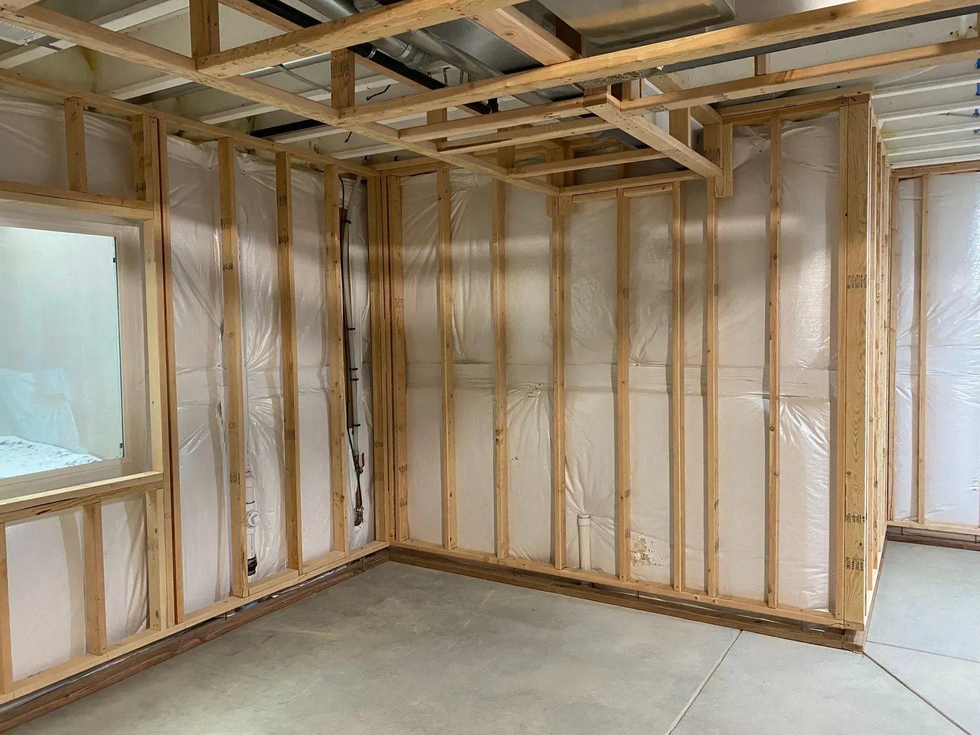 Interior view of a room under construction; wooden studs, plastic sheeting, and unfinished concrete floor.