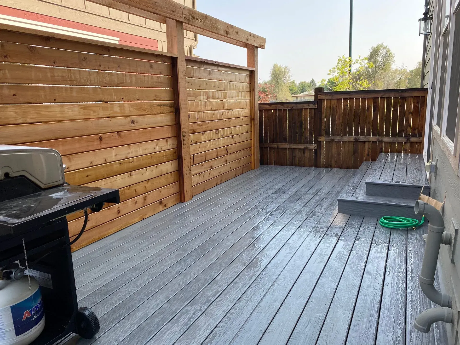 Wooden deck with gray flooring, wooden privacy fence, and a grill.
