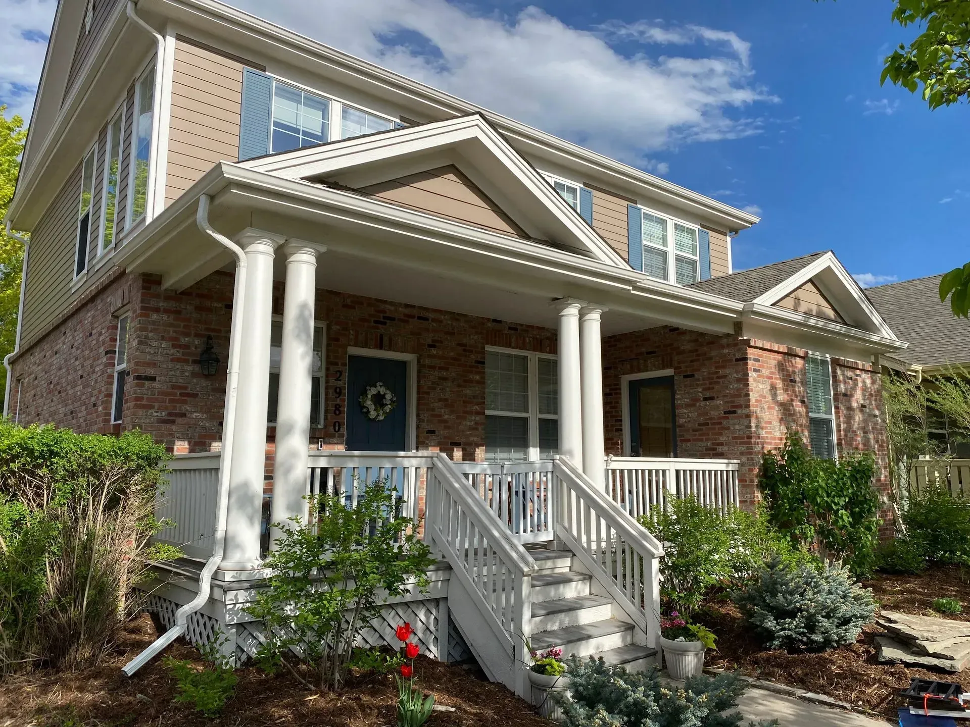 Two-story brick home with white columns, porch, and stairs. Brown siding and blue shutters.