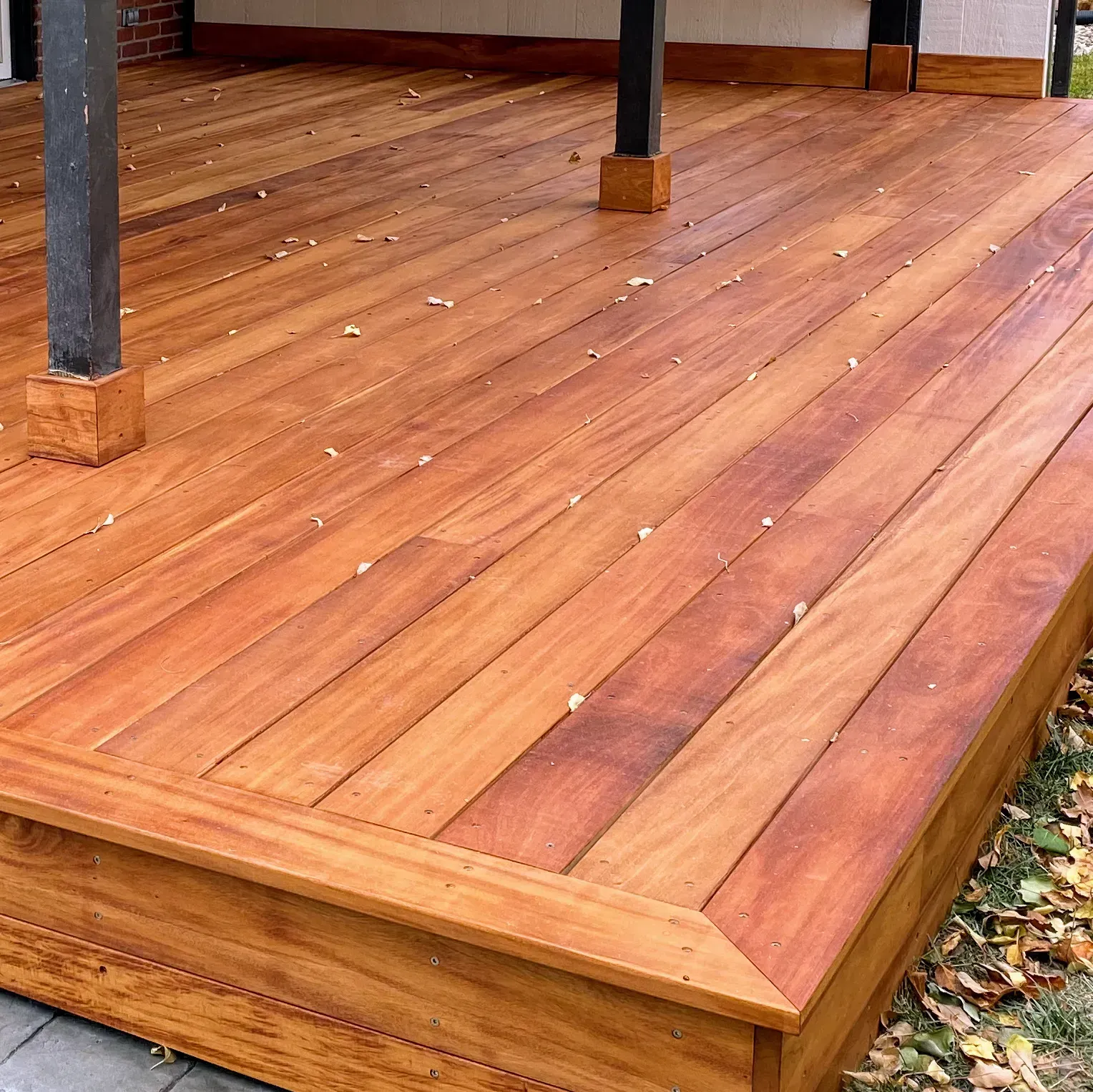 Wooden deck with reddish-brown planks, corner detail visible. Underneath a covered area with black support beams.
