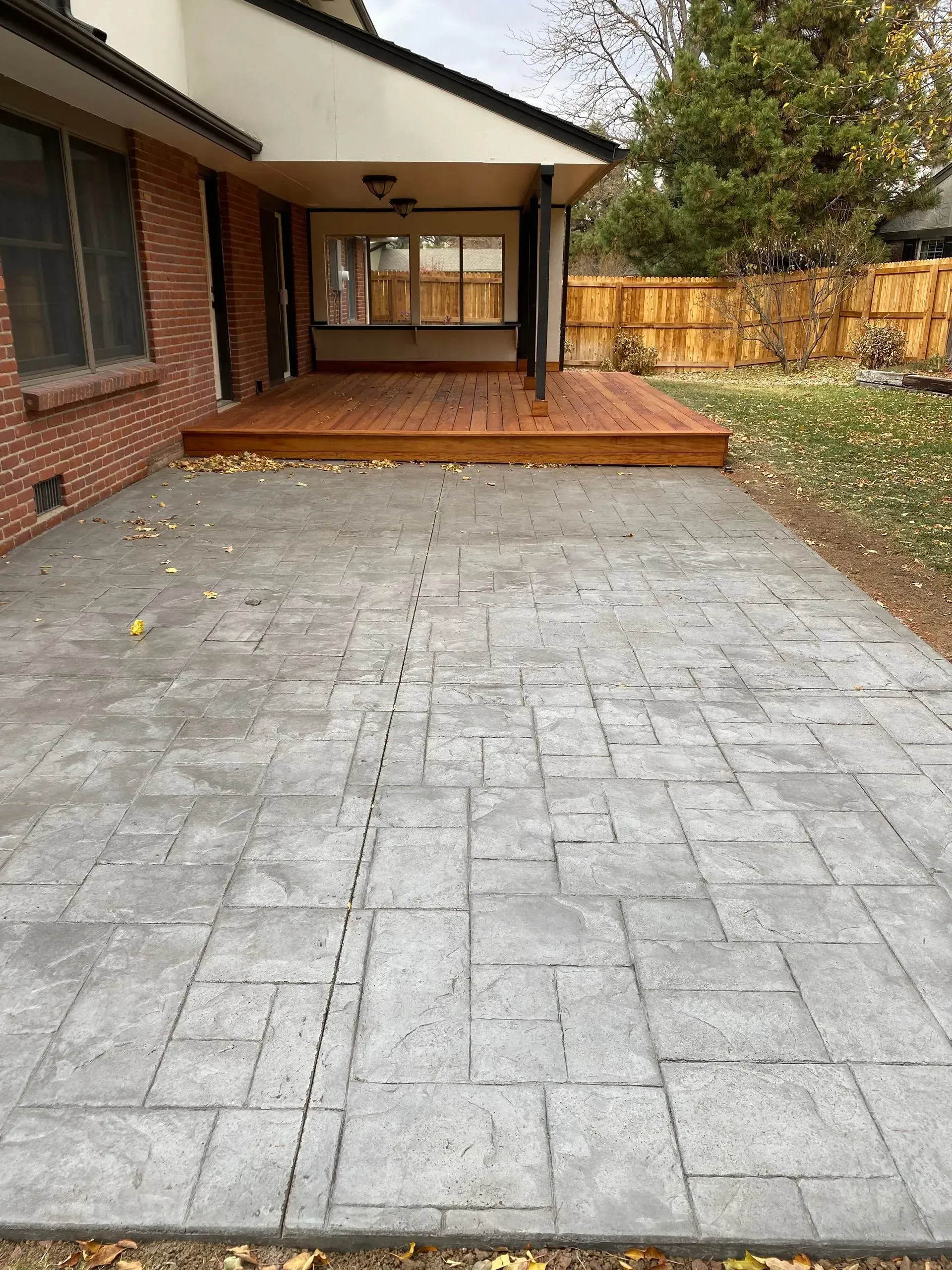 Patio with gray textured concrete leading to a wooden deck under a house's overhang.