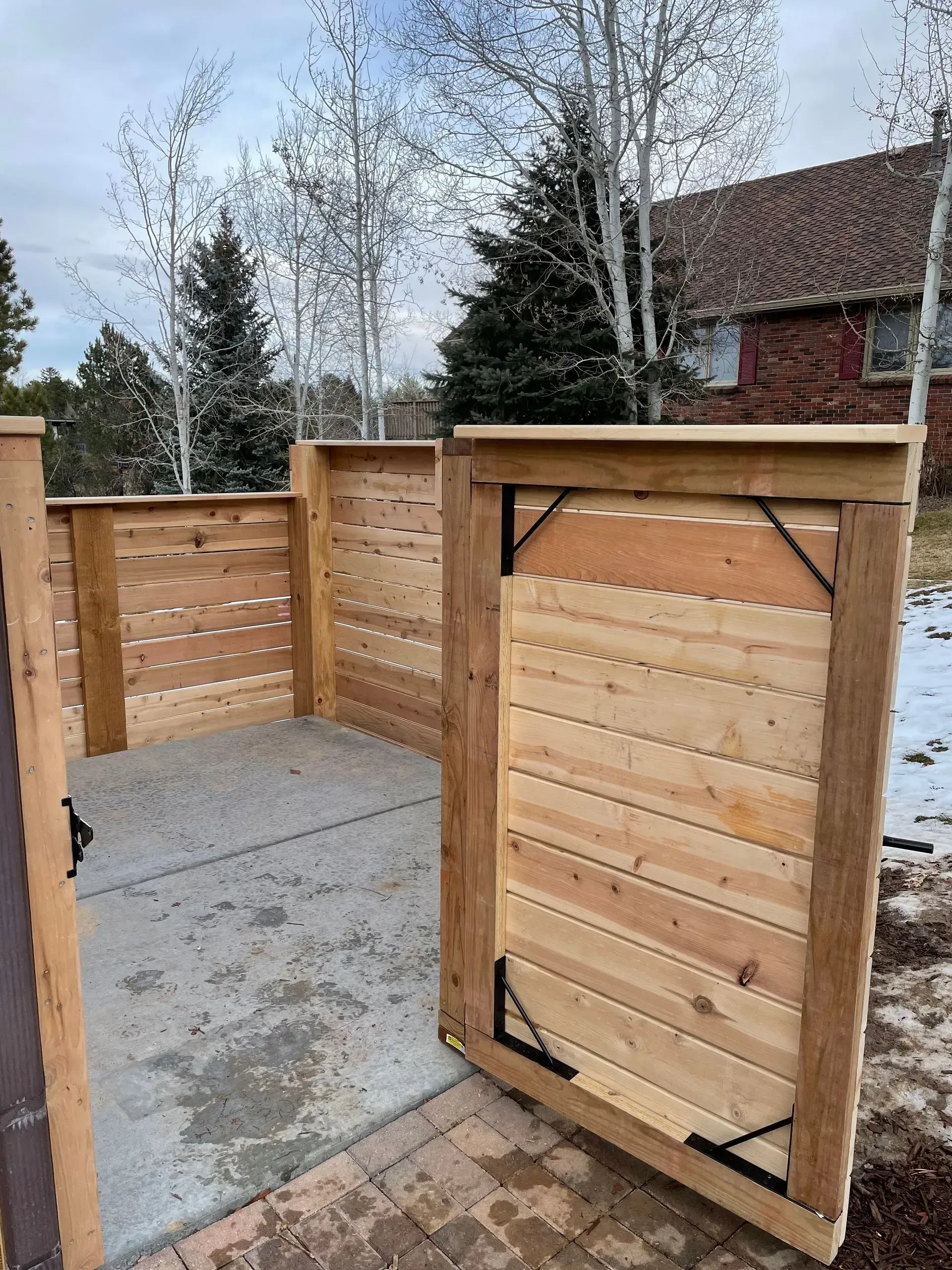 Wooden fence with gate enclosing concrete patio; trees and house in background.