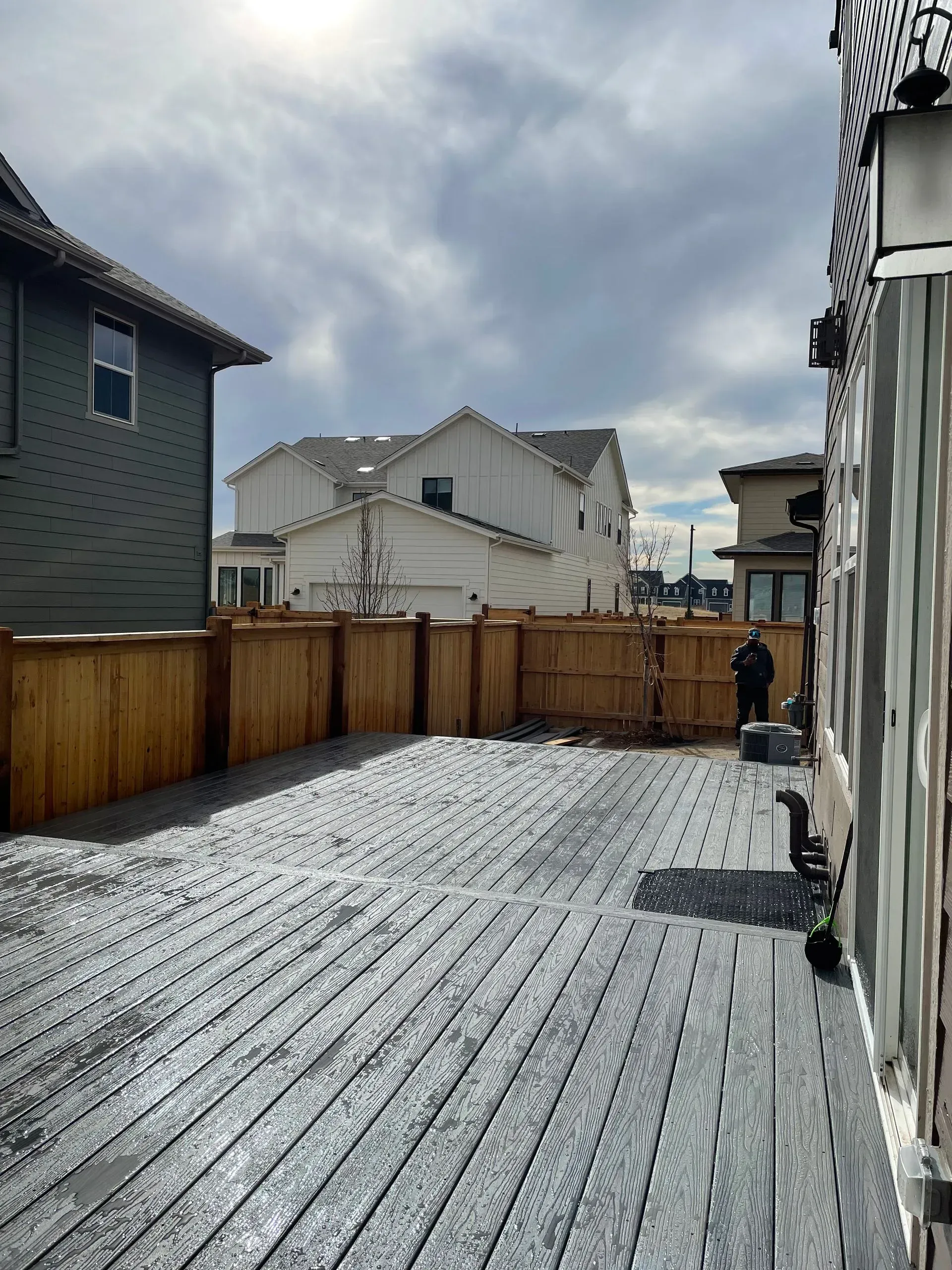 Backyard with wooden fence and gray stone patio, houses in background.