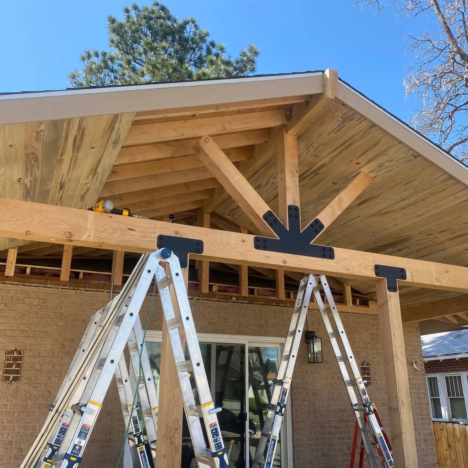 Construction of a covered patio addition on a brick home, with ladders and wooden beams.