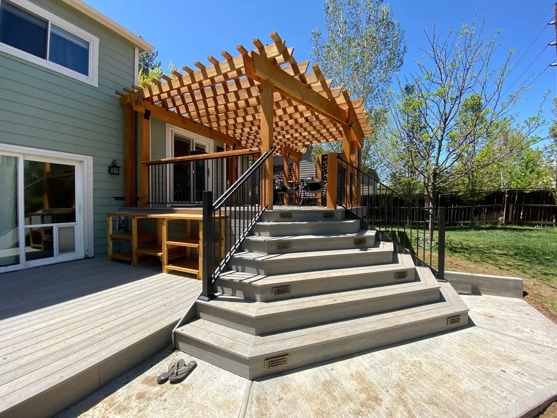 Backyard patio with concrete steps, wooden pergola, and a ramp.