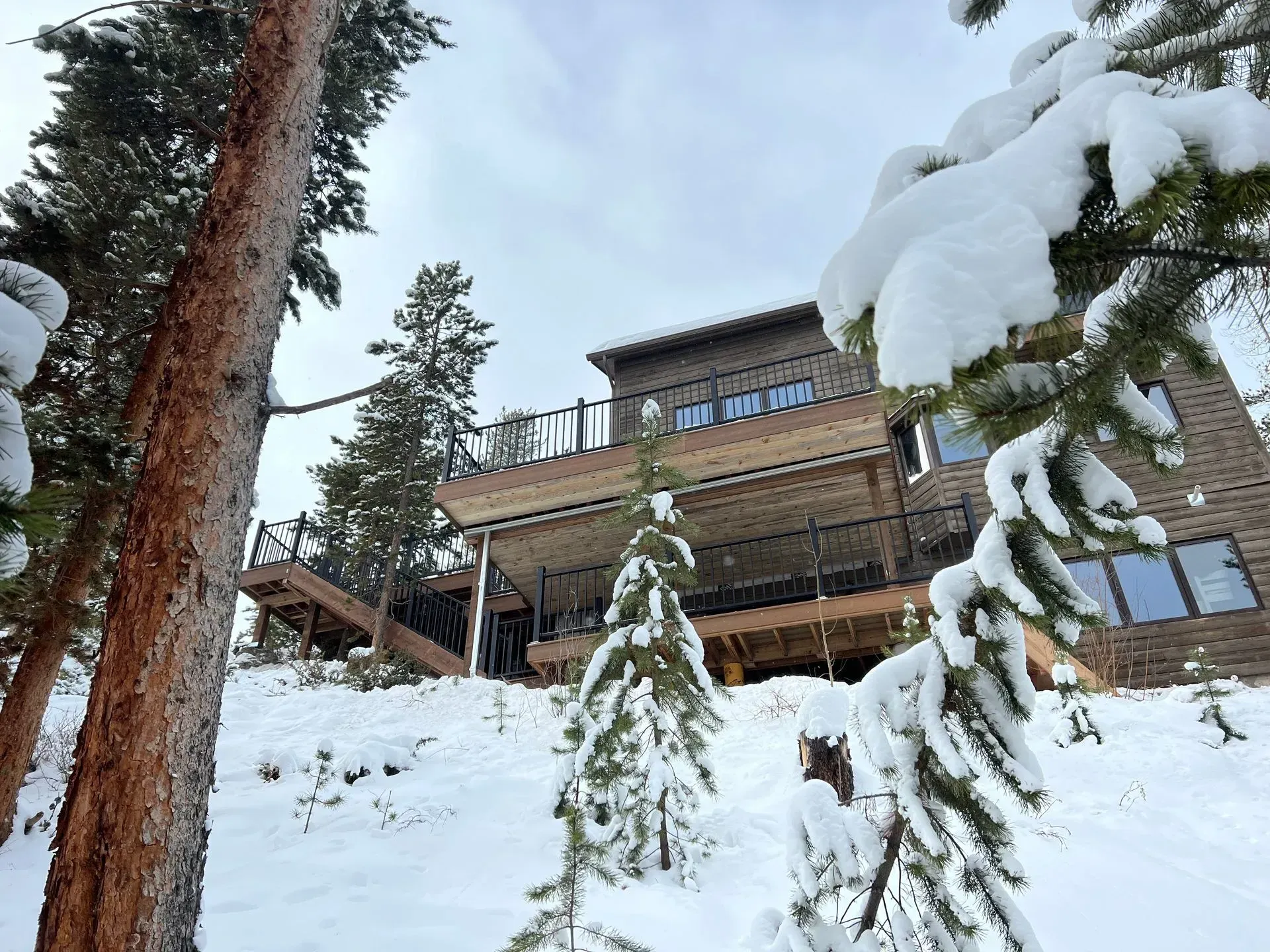Snowy cabin in a wooded area with a deck; overcast sky.