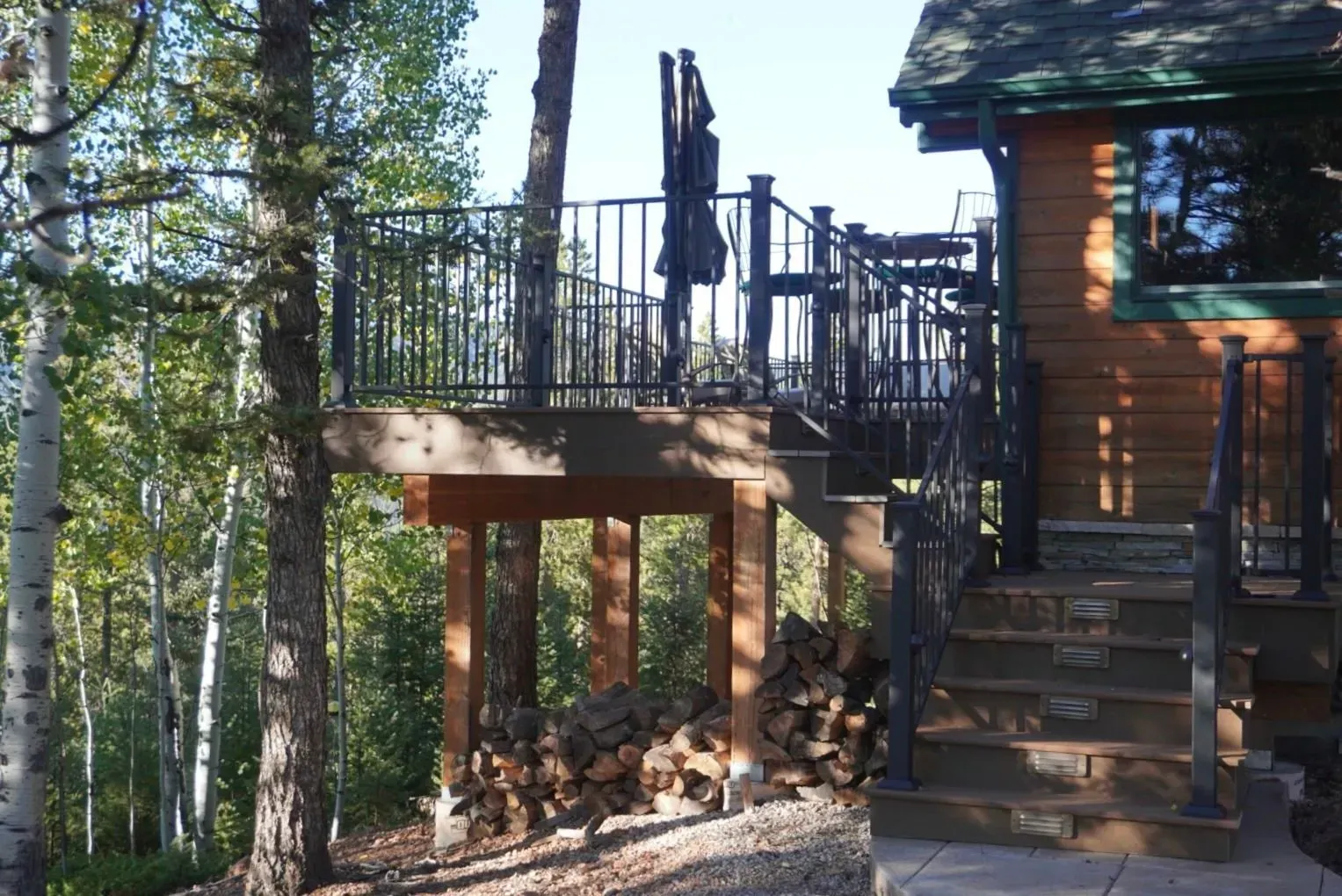 Wooden deck with stairs next to a cabin; firewood below the deck.