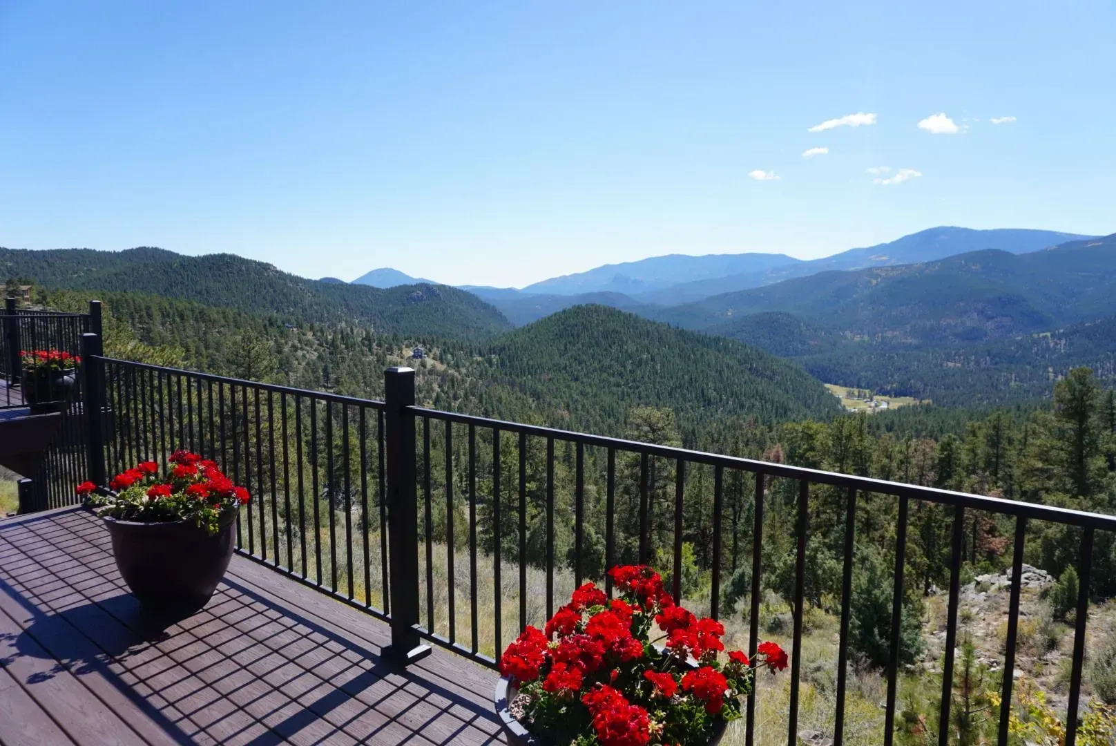 Deck overlooking mountain range with red flower pots.
