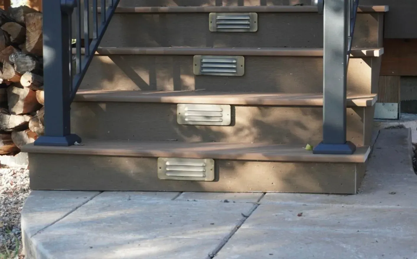 Outdoor staircase with built-in lights. Brown steps, black railing, concrete landing.