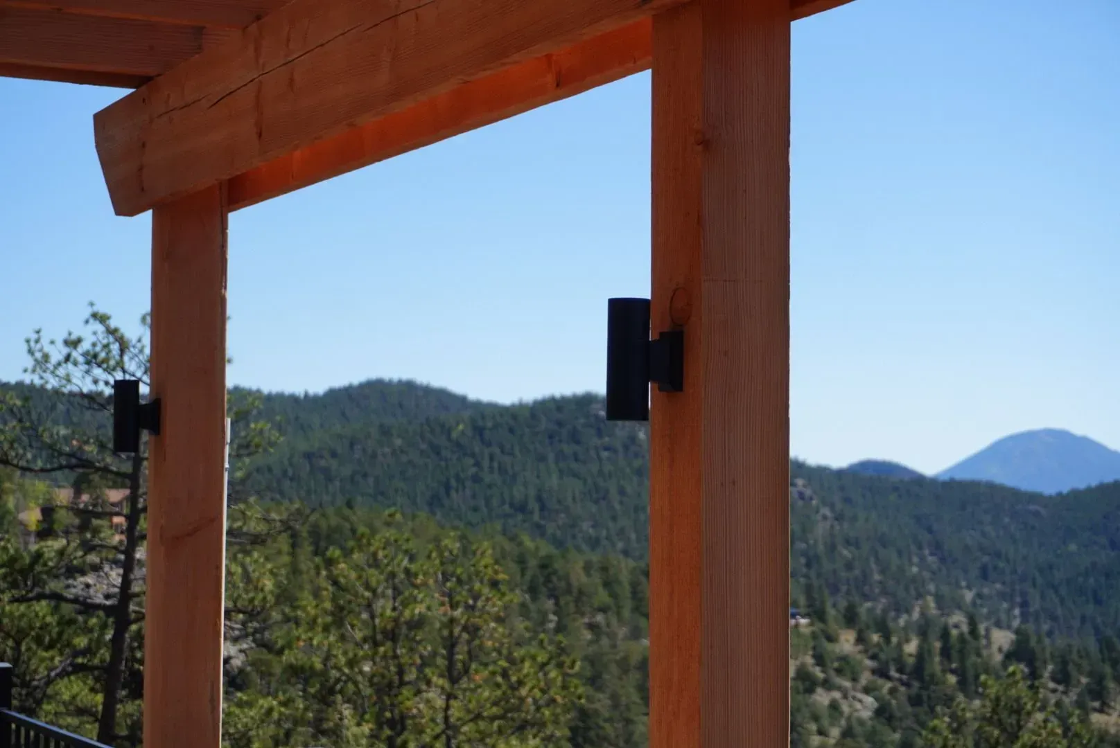 Wooden beams frame a scenic mountain view; black sconce lights are mounted on the posts.